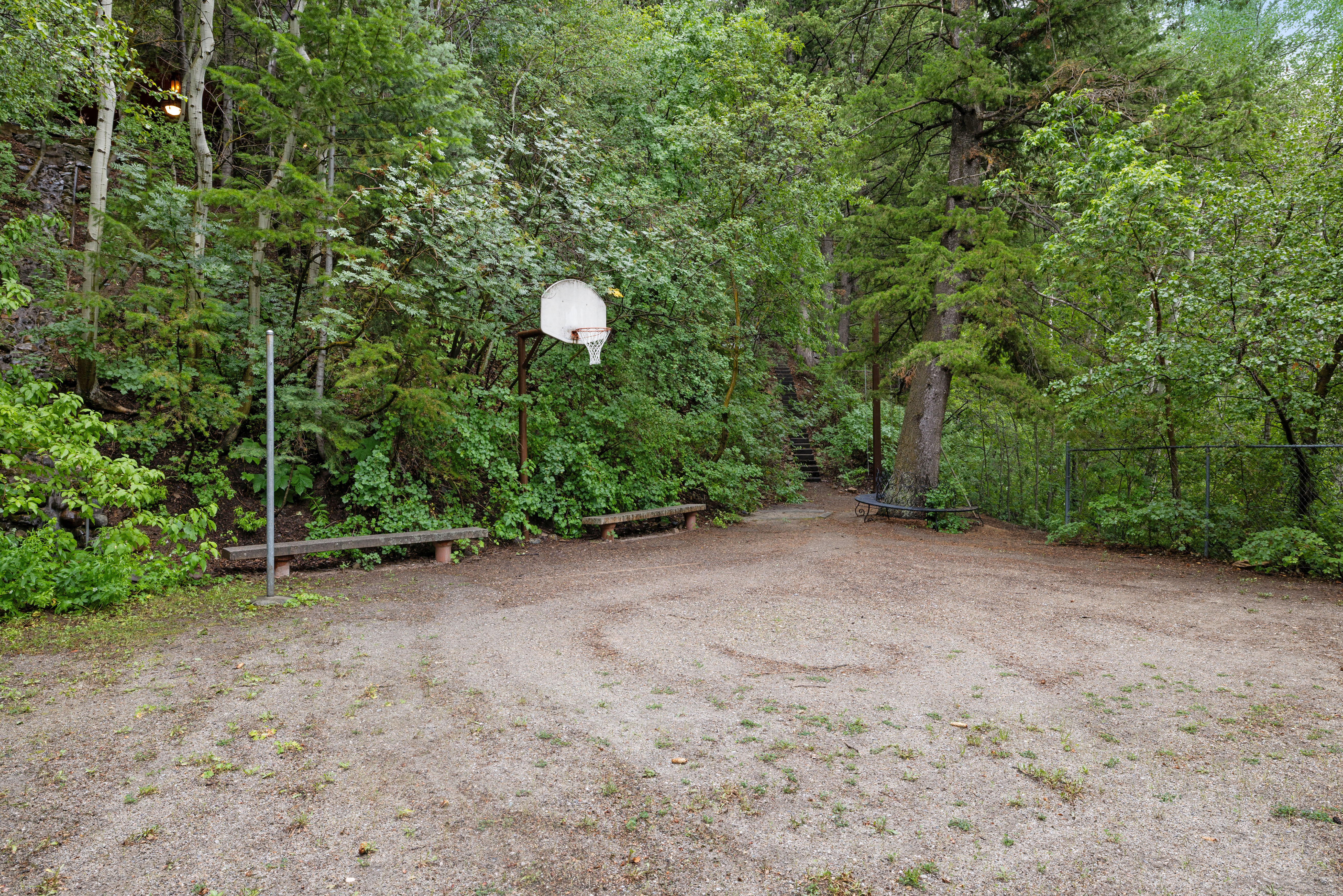 Outdoor recreational area featuring a basketball hoop and volleyball court, two benches, and a flat surface.