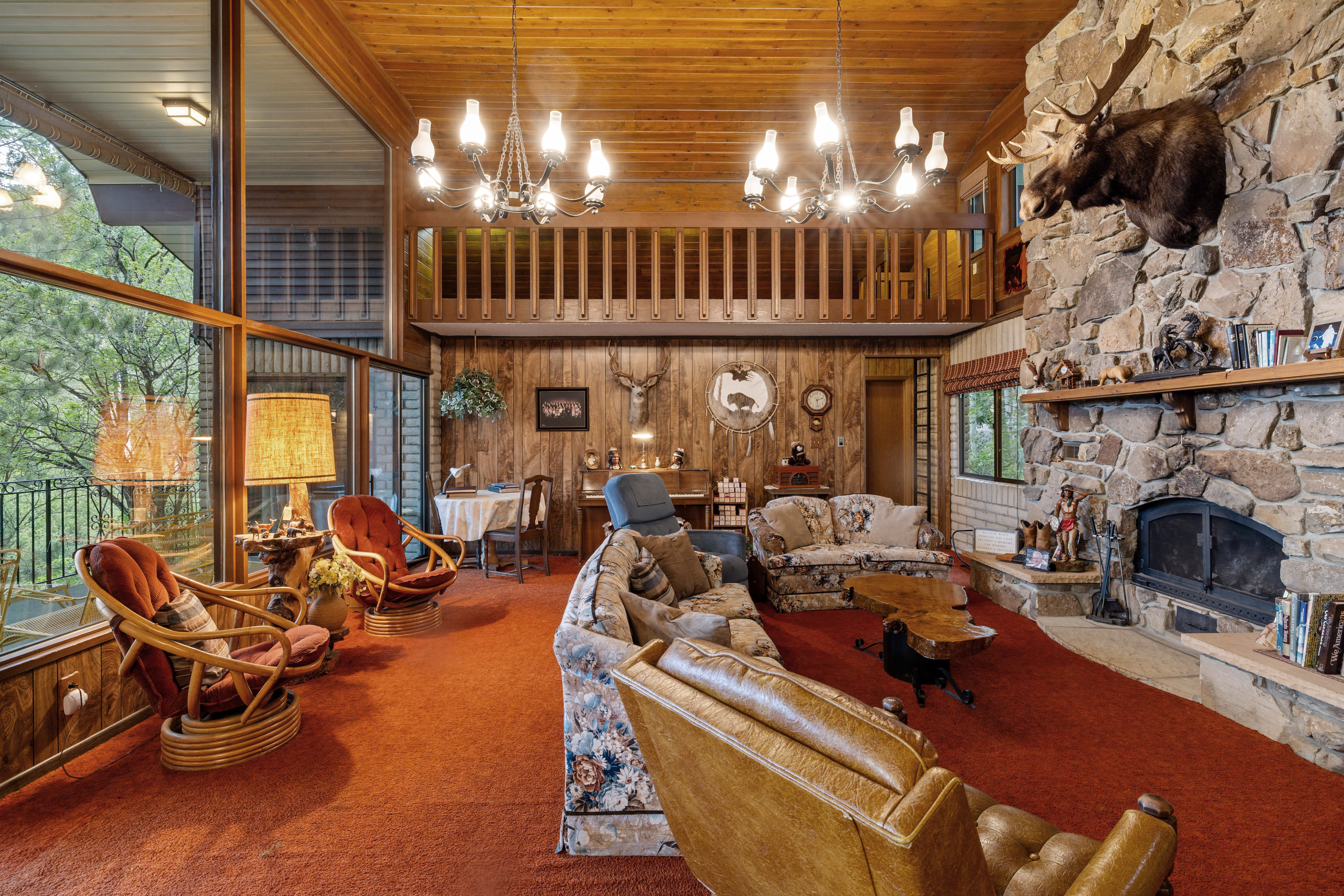 Spacious living area featuring a floor-to-ceiling stone fireplace, wood-plank ceilings, and a second-story loft.