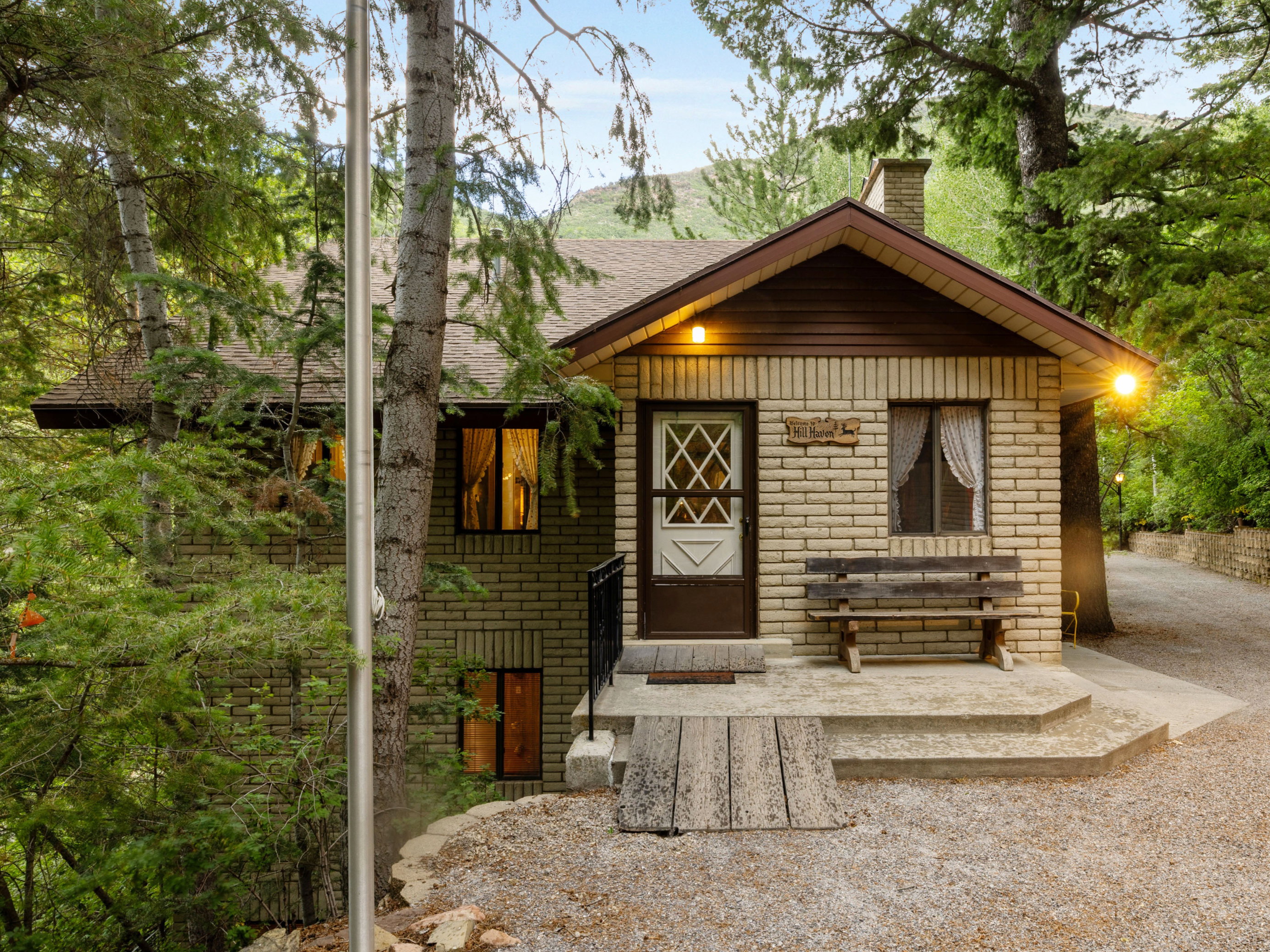Brick exterior construction, prominent gravel driveway, established trees, and surrounding natural foliage