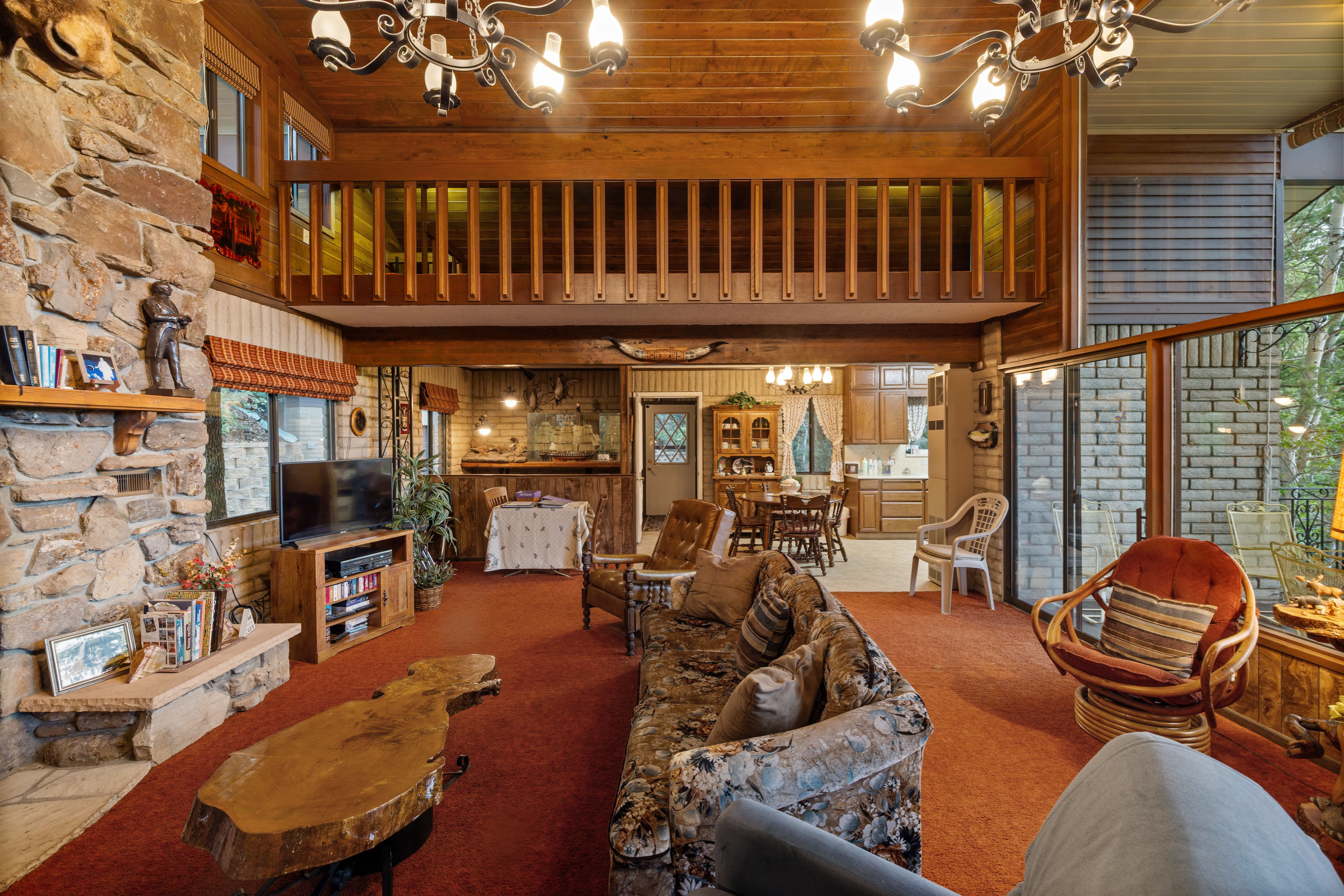 Spacious living area featuring a floor-to-ceiling stone fireplace, wood-plank ceilings, and a second-story loft with wood railing
