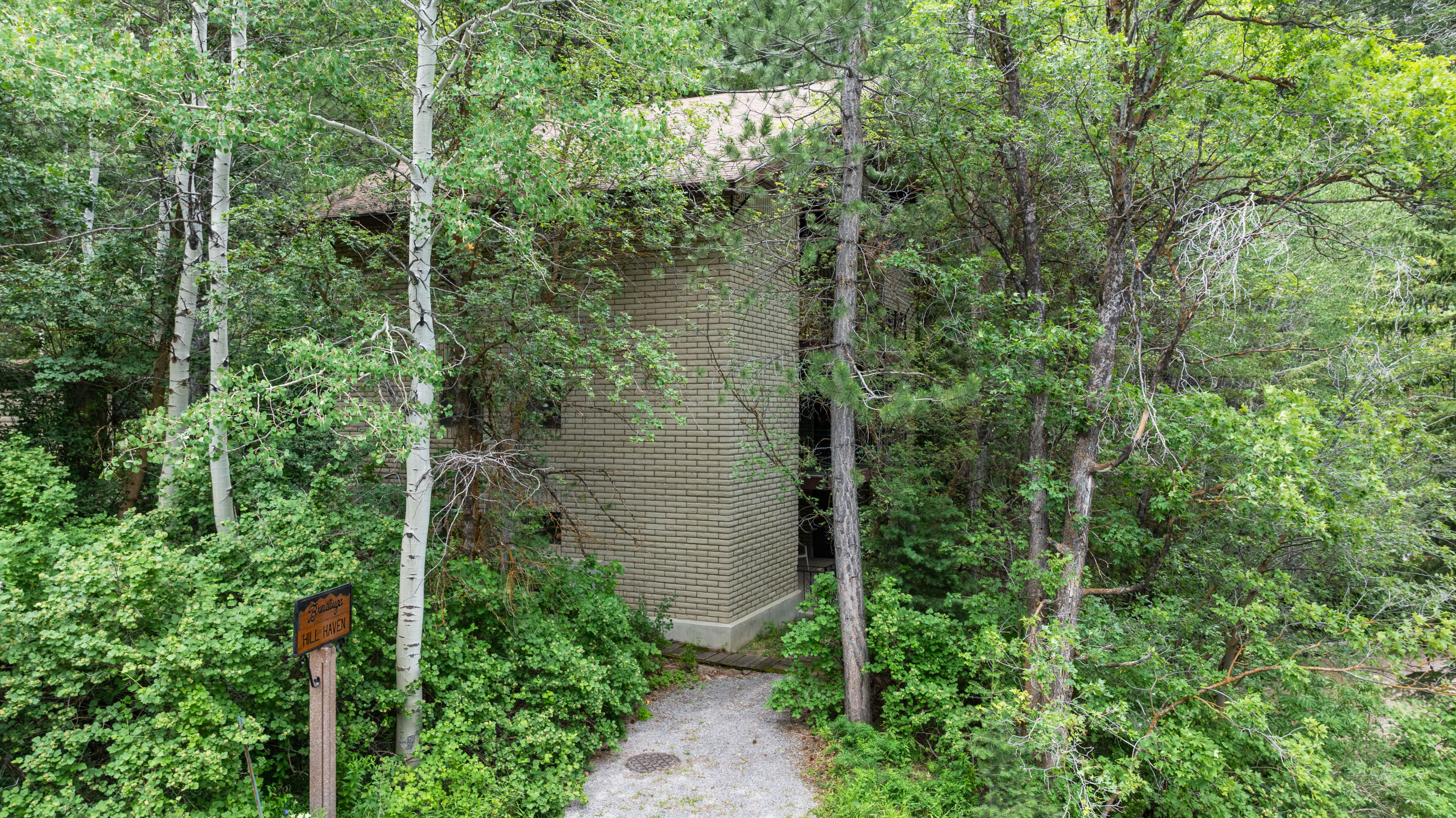 Brick exterior cabin surrounded by mature deciduous trees and lush vegetation