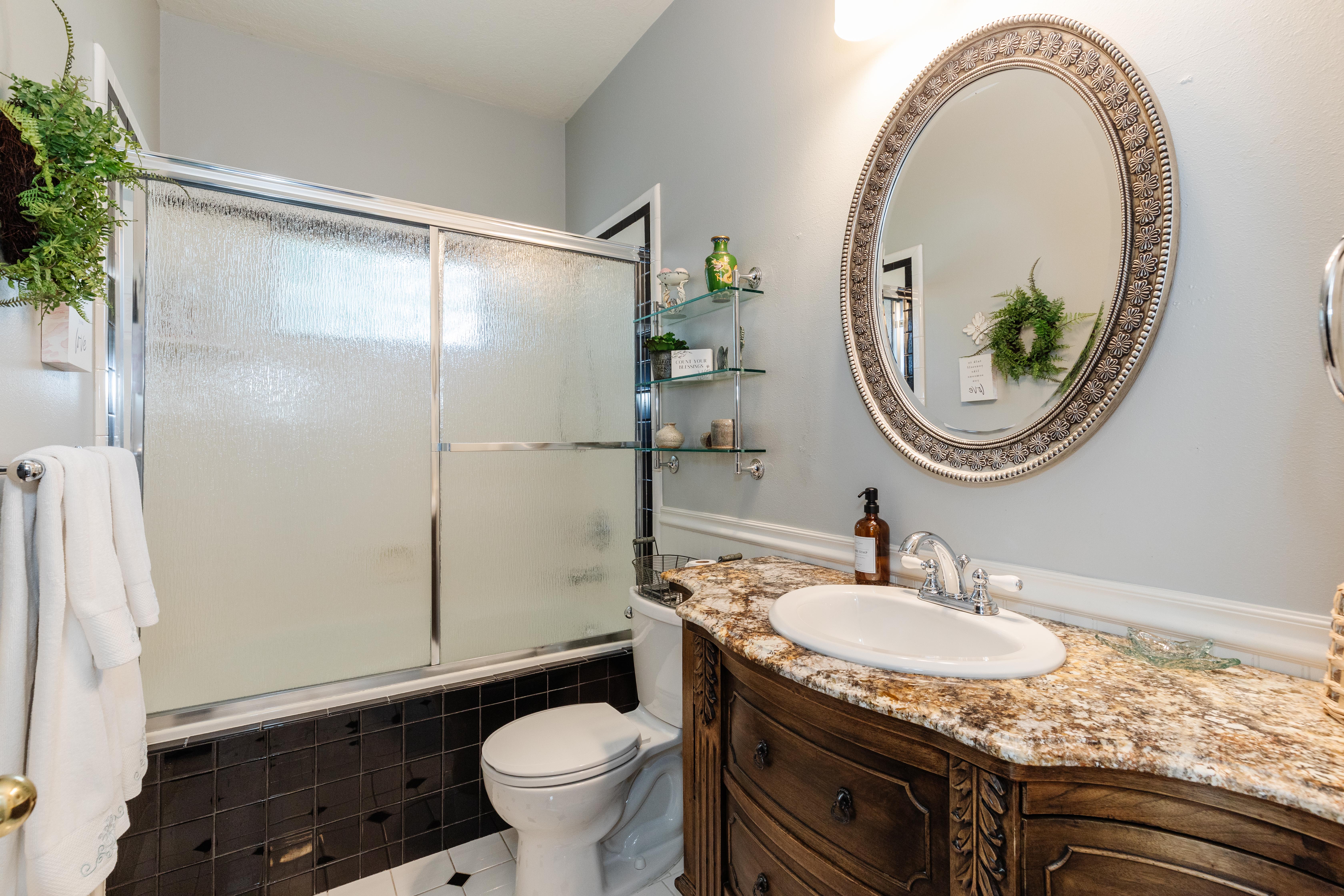 Bathroom featuring a vanity with a stone countertop, an oval mirror, a shower with sliding frosted glass doors, and black and white floor tiling