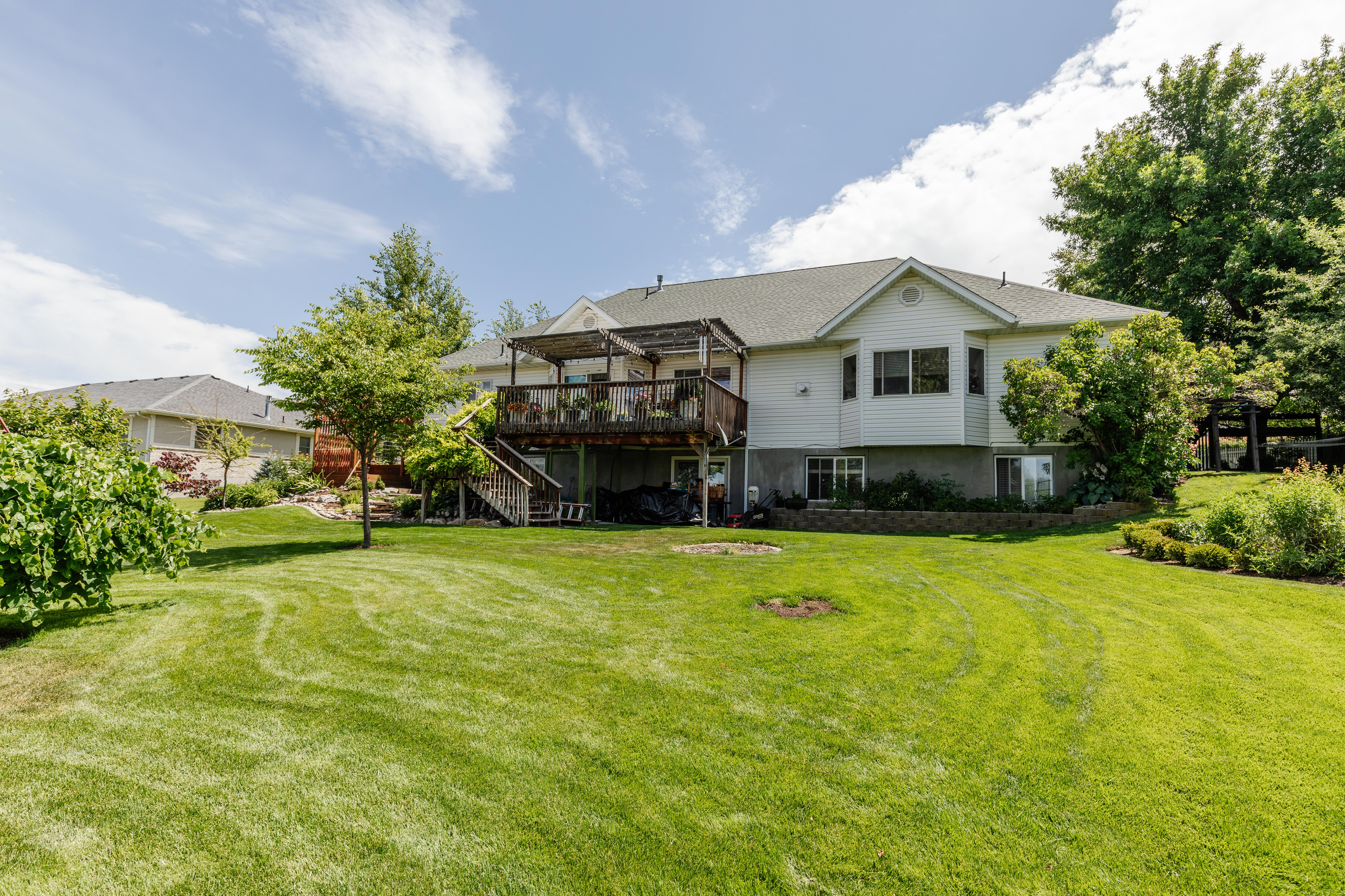 Expansive green lawn with mature trees and a multi-level deck featuring a pergola
