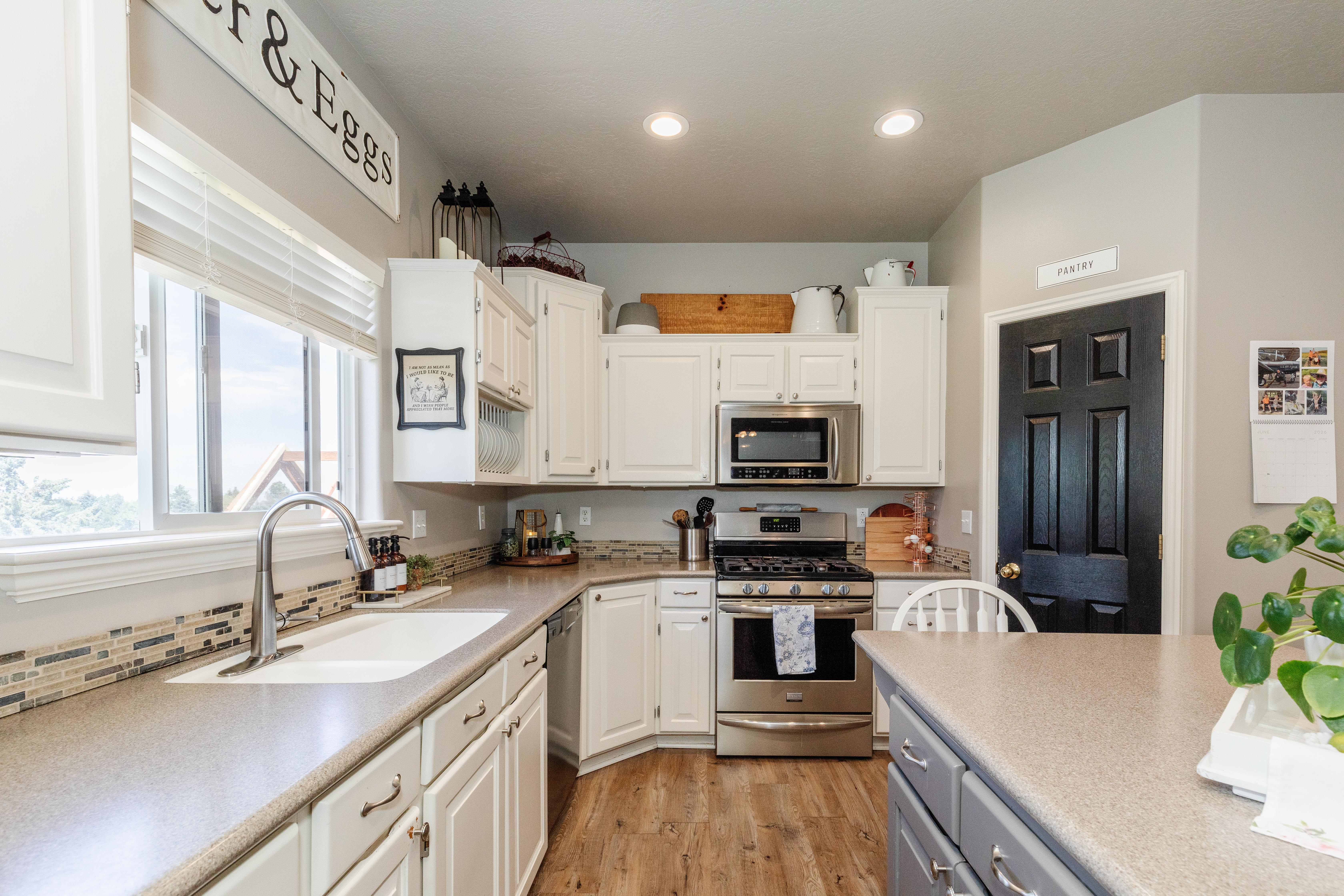 Kitchen featuring white cabinetry with brushed nickel hardware, stainless steel appliances, a composite sink with a gooseneck faucet, and wood-finish flooring