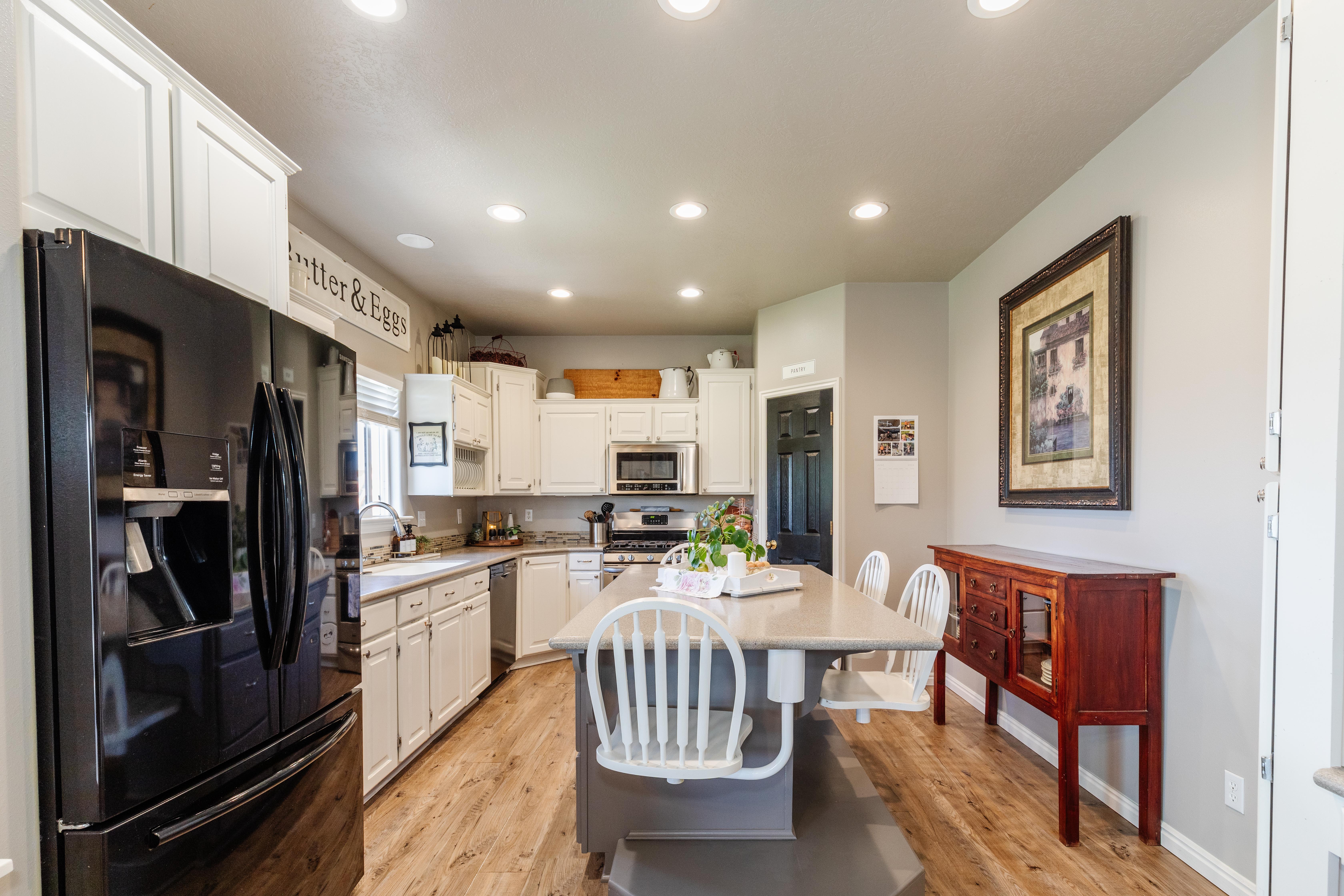 Open-concept kitchen featuring an oversized island with seating, wood-finish flooring, white cabinetry, integrated stainless steel appliances, and recessed lighting