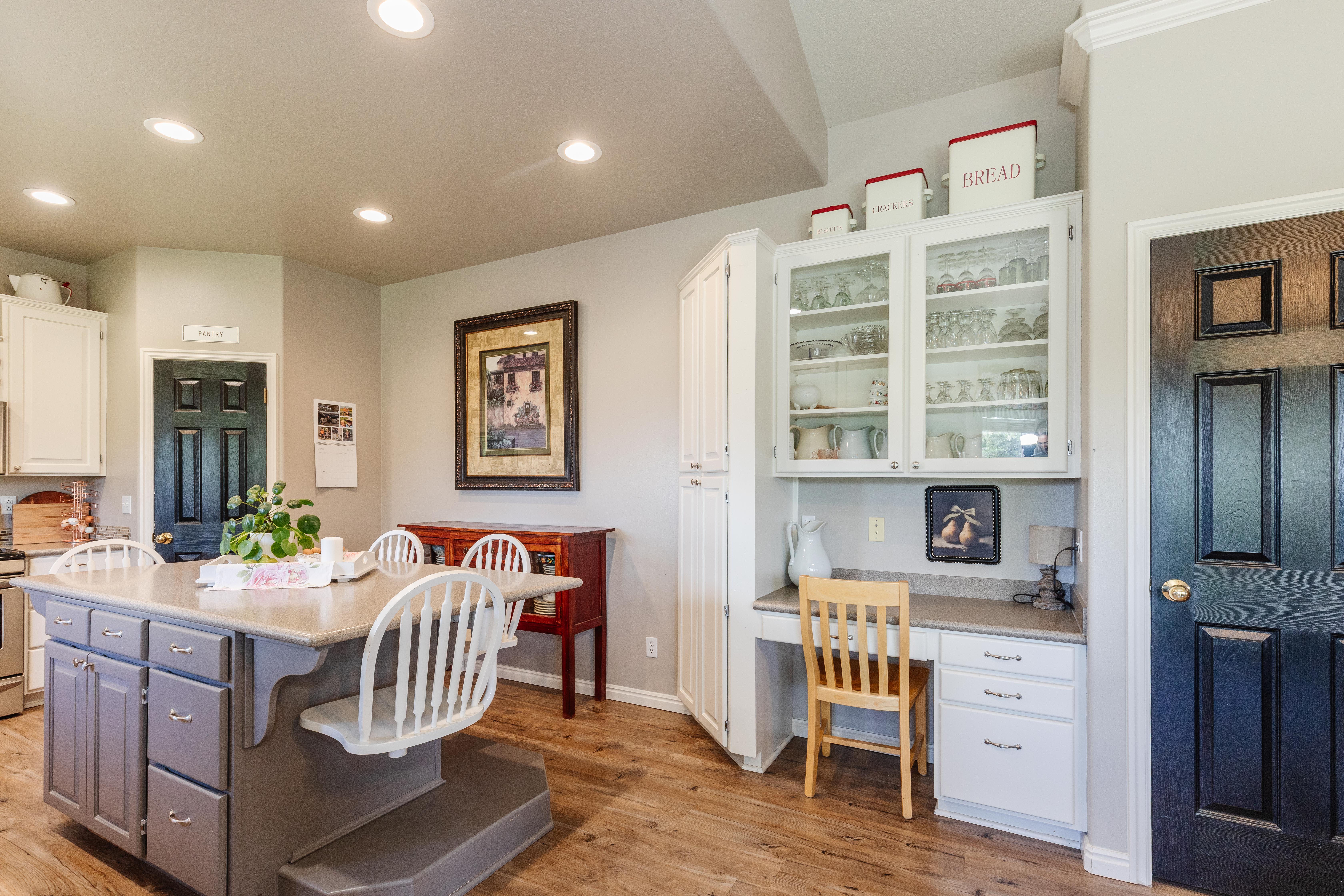 Kitchen featuring a center island with integrated seating, wood-finish flooring, recessed lighting, built-in desk with overhead glass-front cabinetry, and white paneled cabinetry