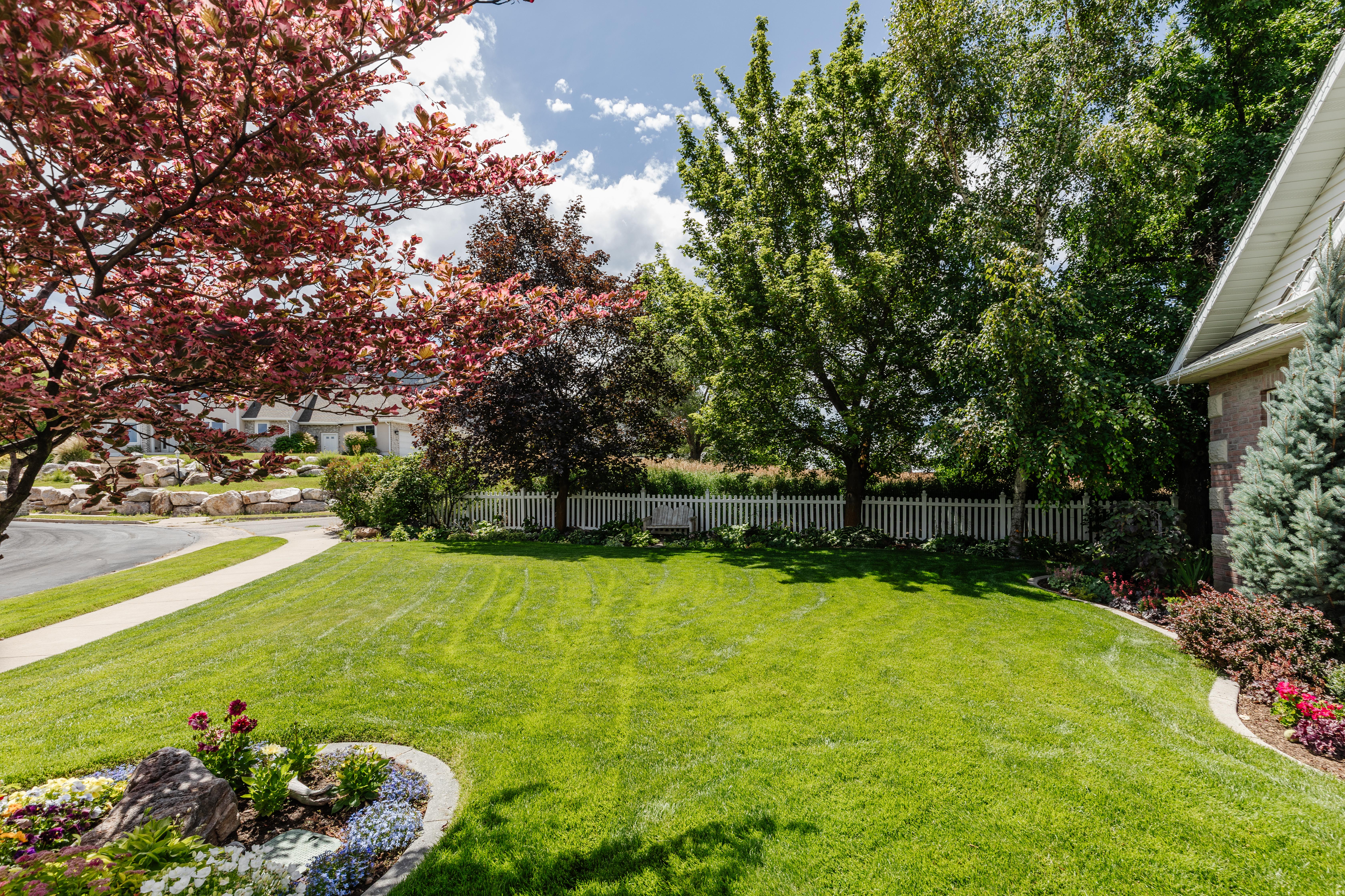 Expansive front lawn with mature trees and a decorative flower bed