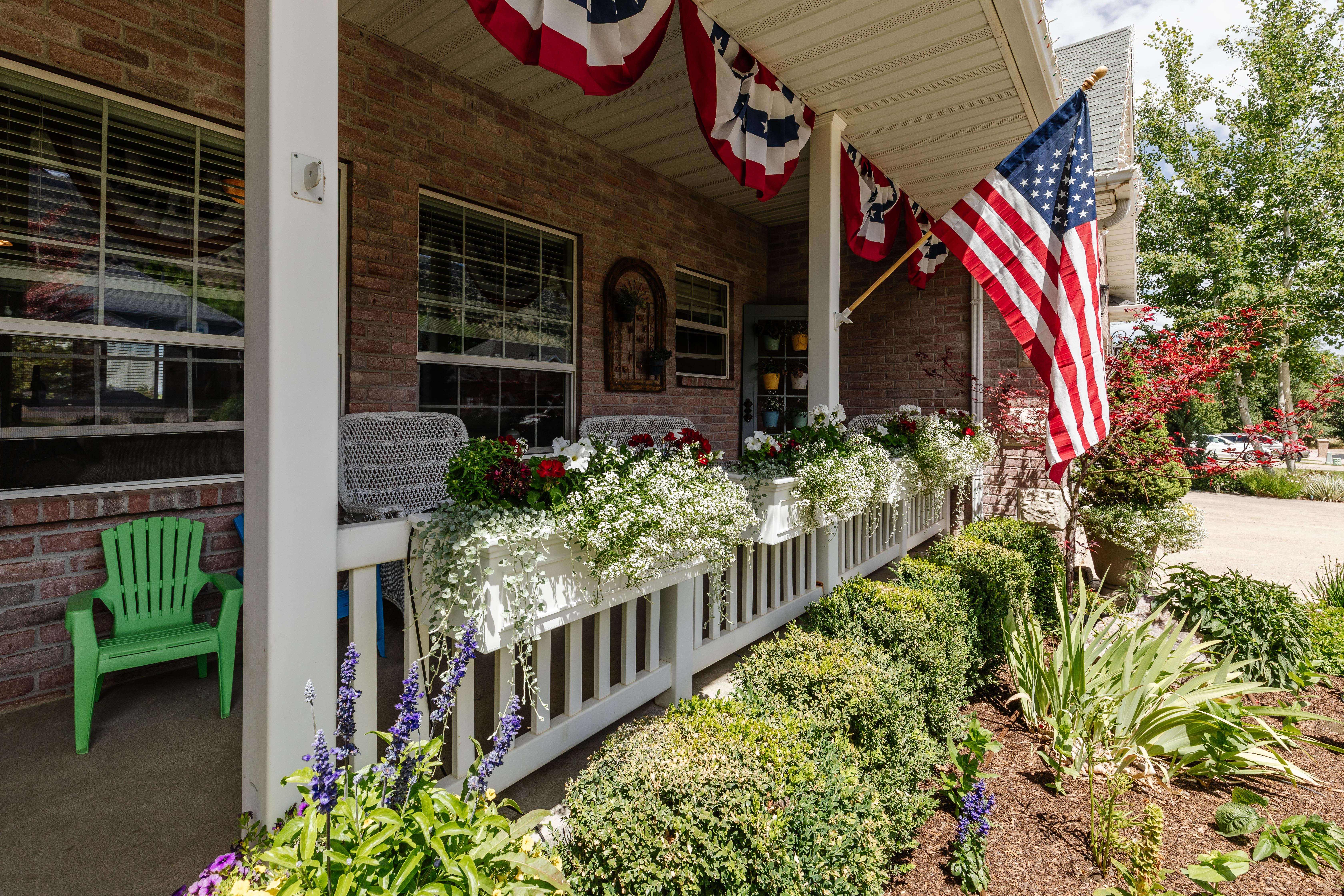 Brick exterior featuring a covered porch with white columns, a white railing, and multiple window boxes
