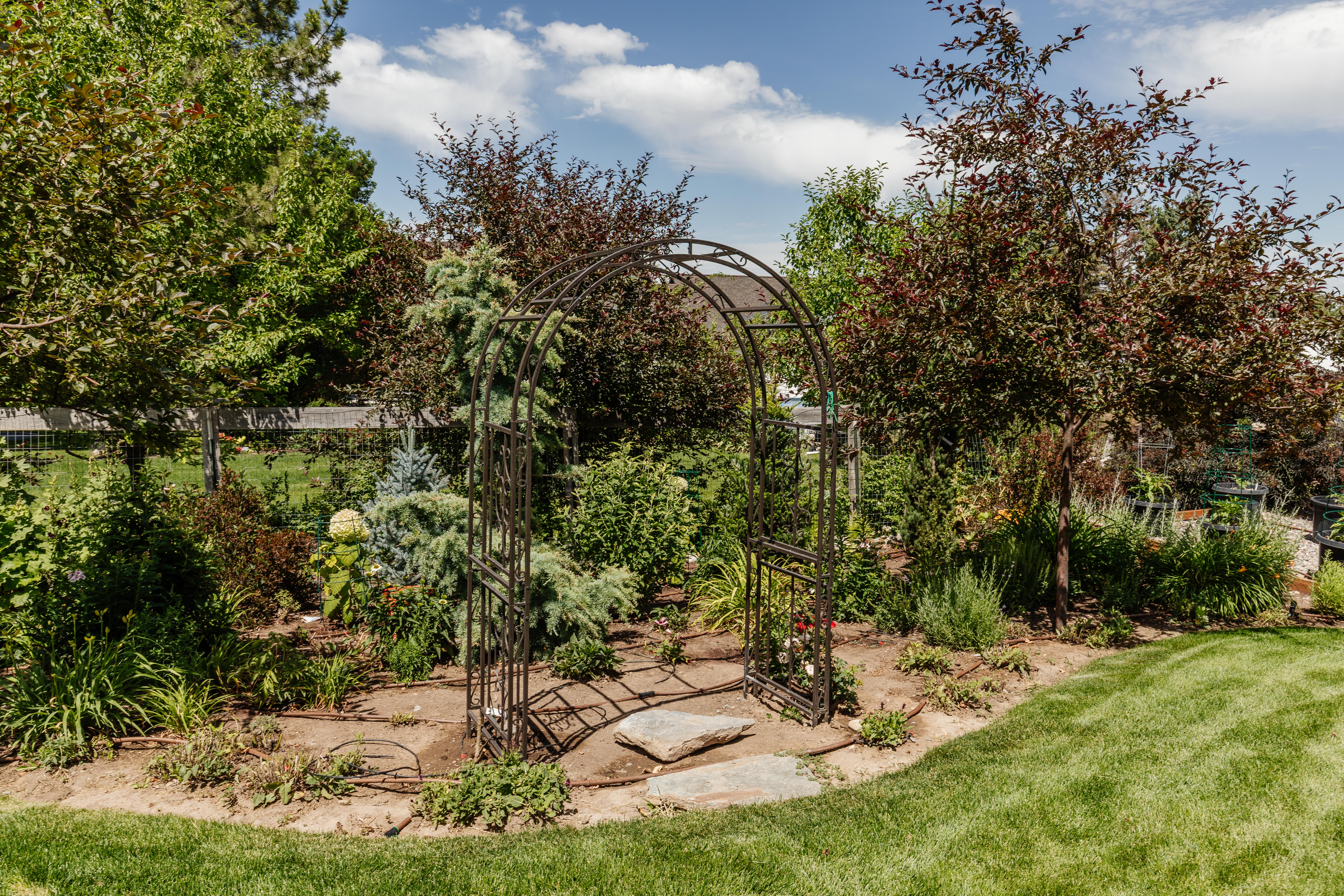 Expansive landscaped garden featuring a decorative metal archway, mature trees, and varied plantings