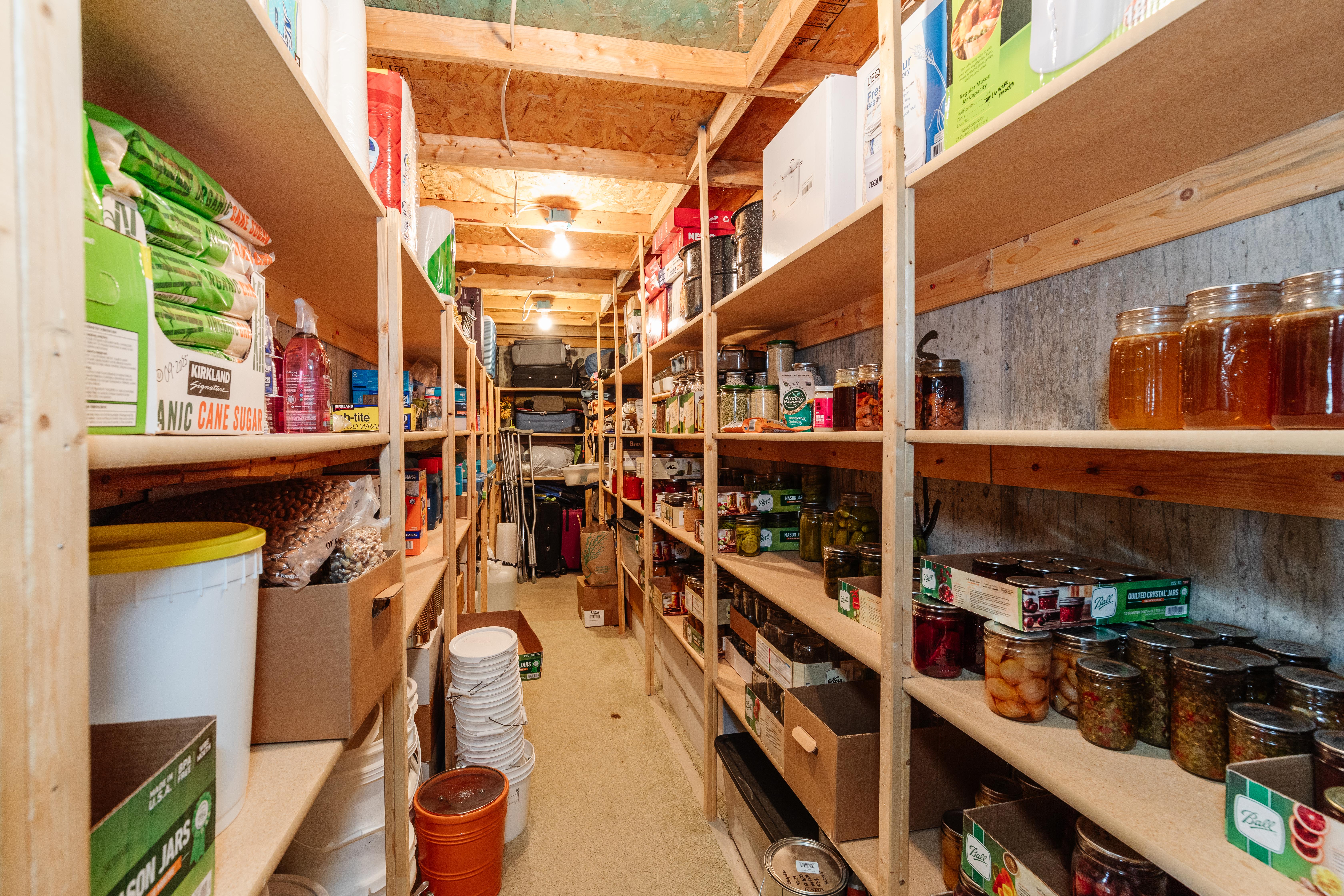 Extensive storage room featuring multiple rows of built-in wooden shelving, exposed wood ceiling joists, and overhead lighting