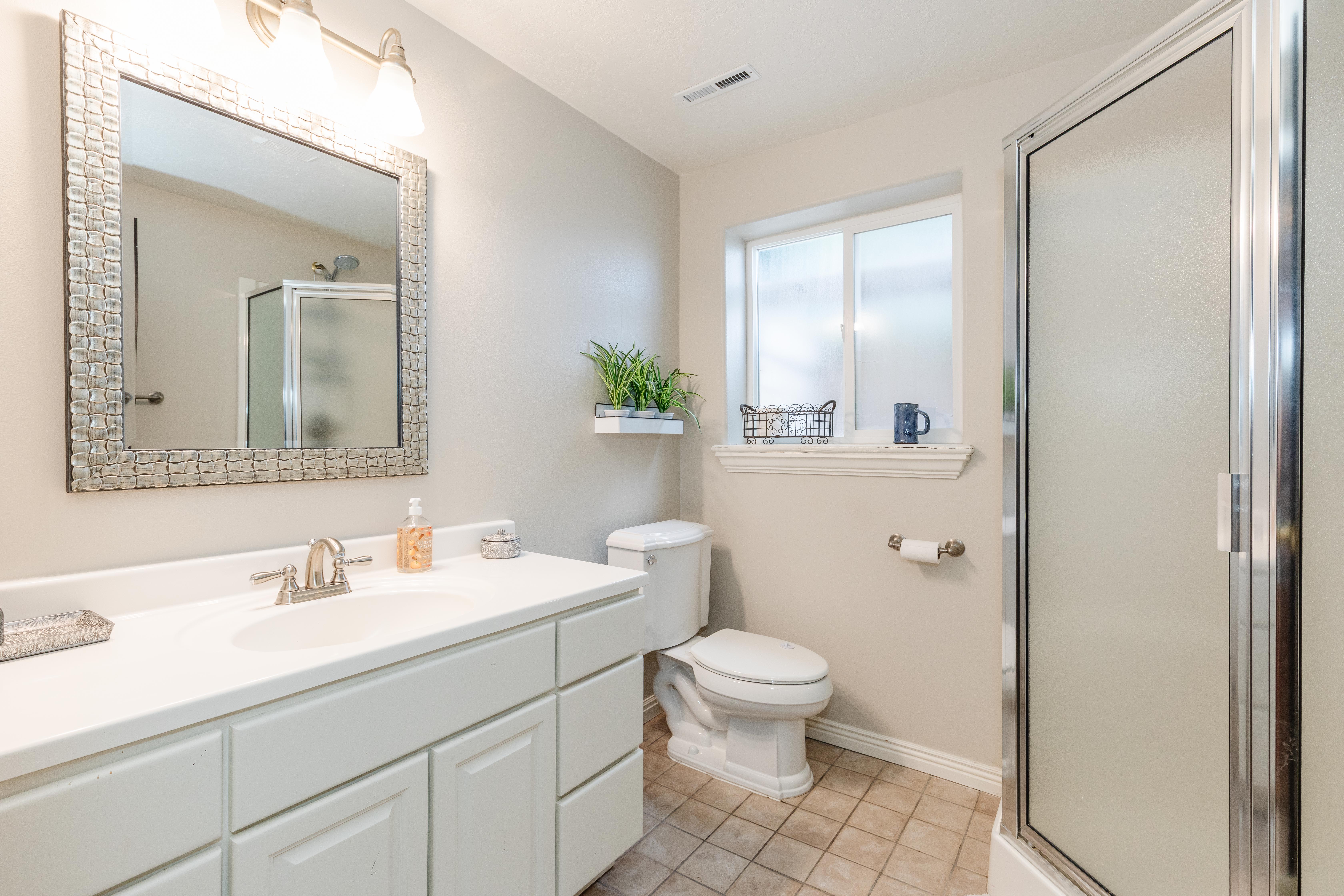 Bathroom featuring a vanity with a white countertop and integrated sink, a framed mirror, and a shower with a frosted glass enclosure