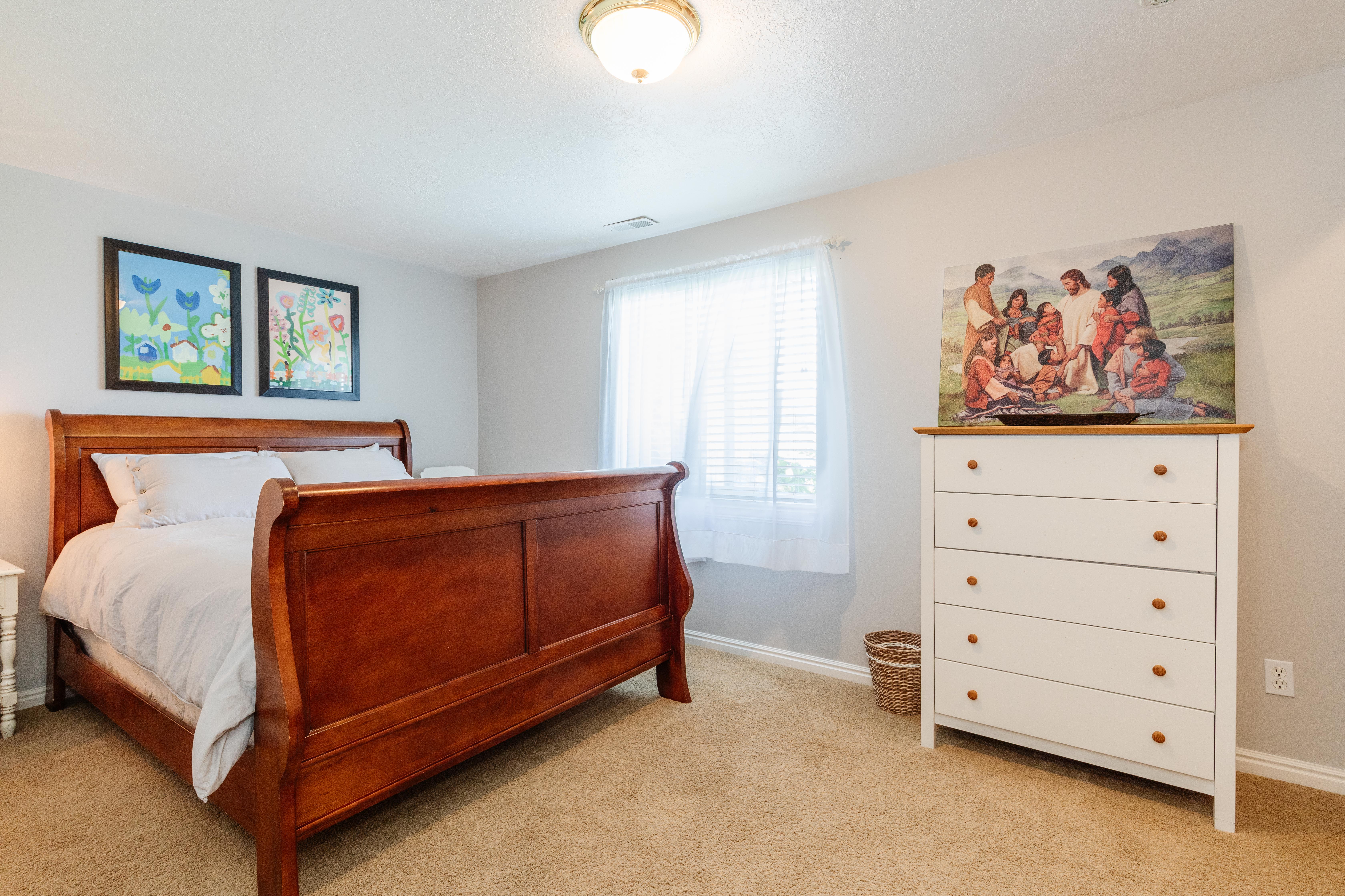Carpeted bedroom with neutral wall tones and a window featuring blinds and sheer curtains