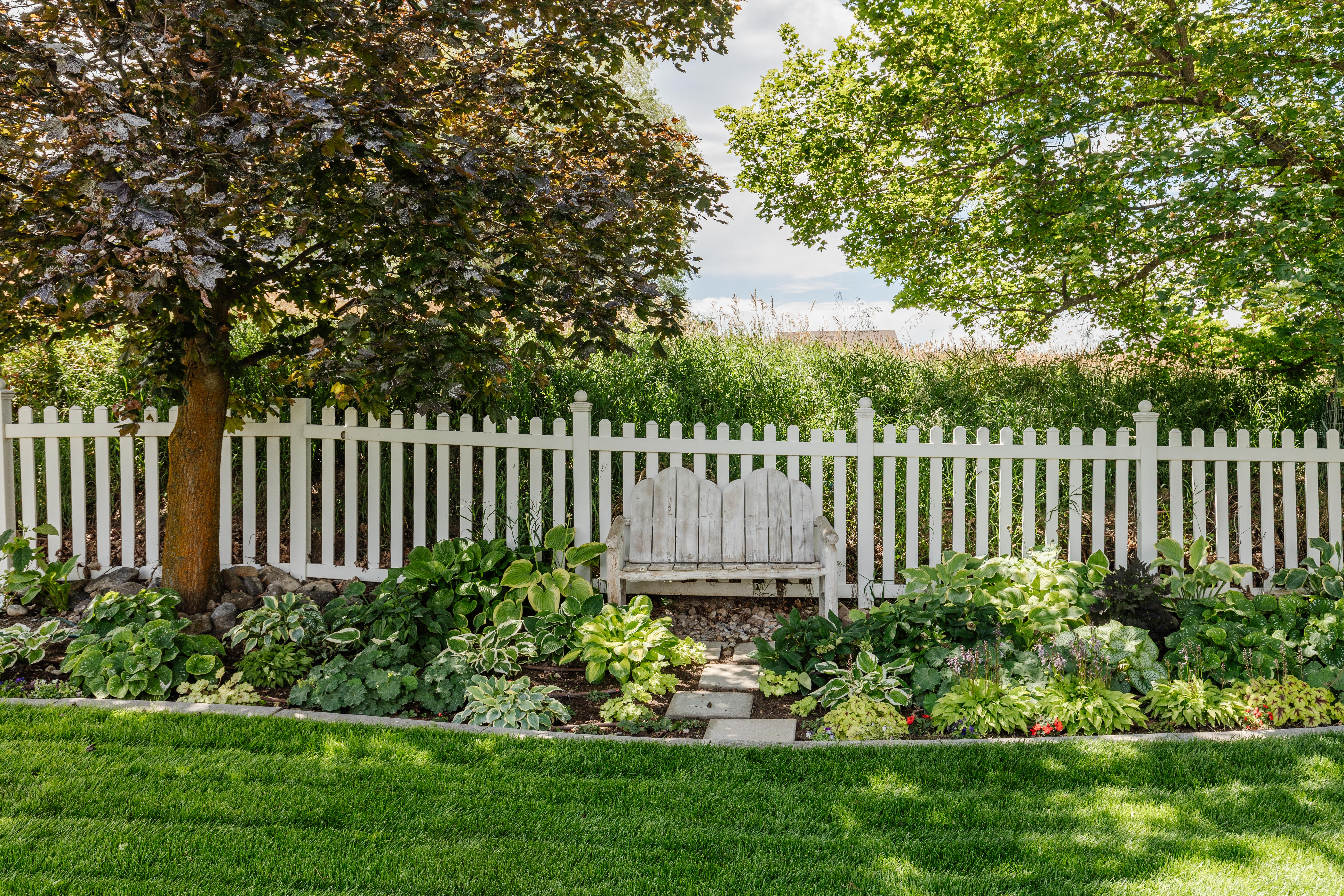 Manicured lawn with a white picket fence, mature trees, and diverse landscaping