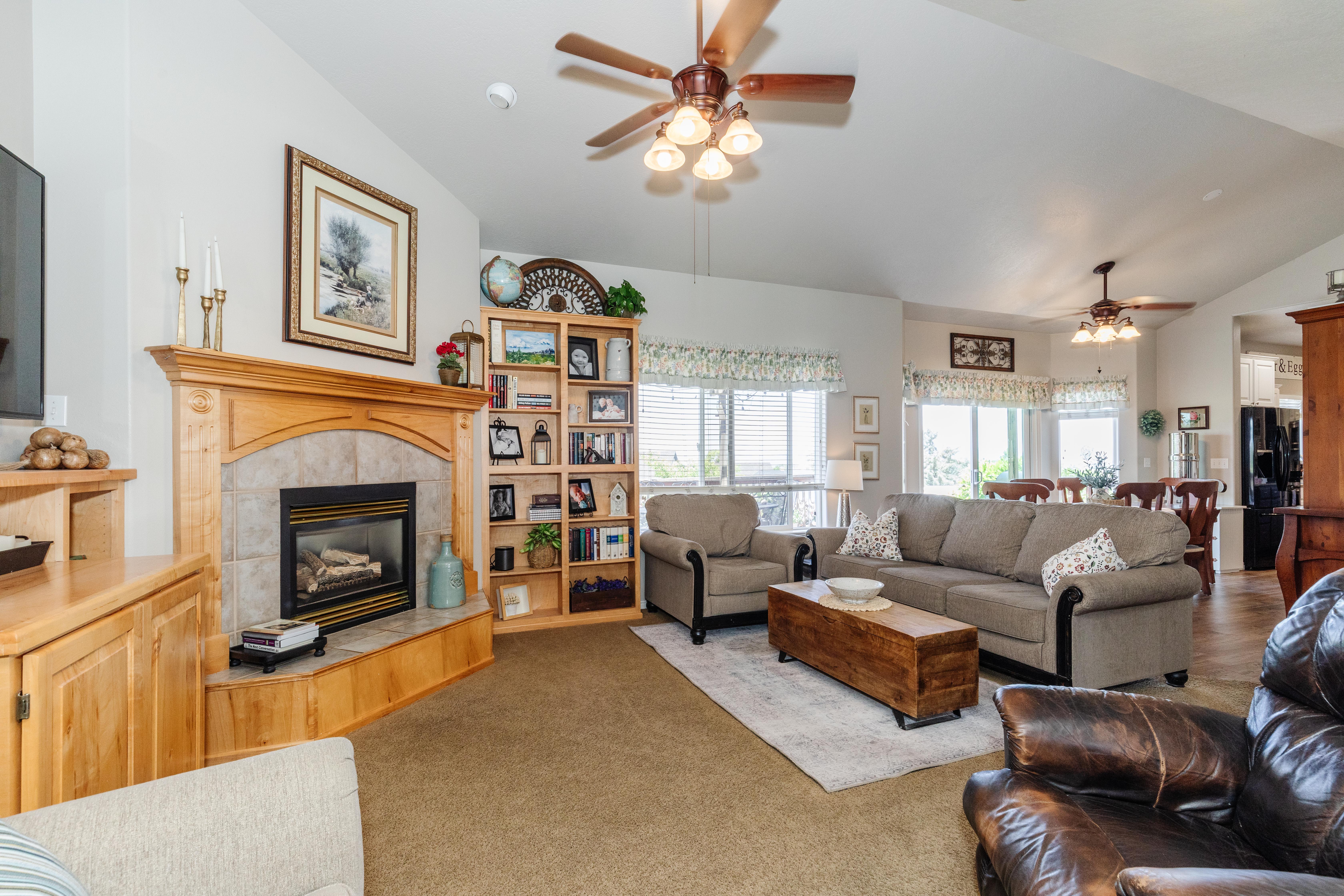 Living room featuring a light wood mantel with a tiled fireplace, vaulted ceilings, and ceiling fans