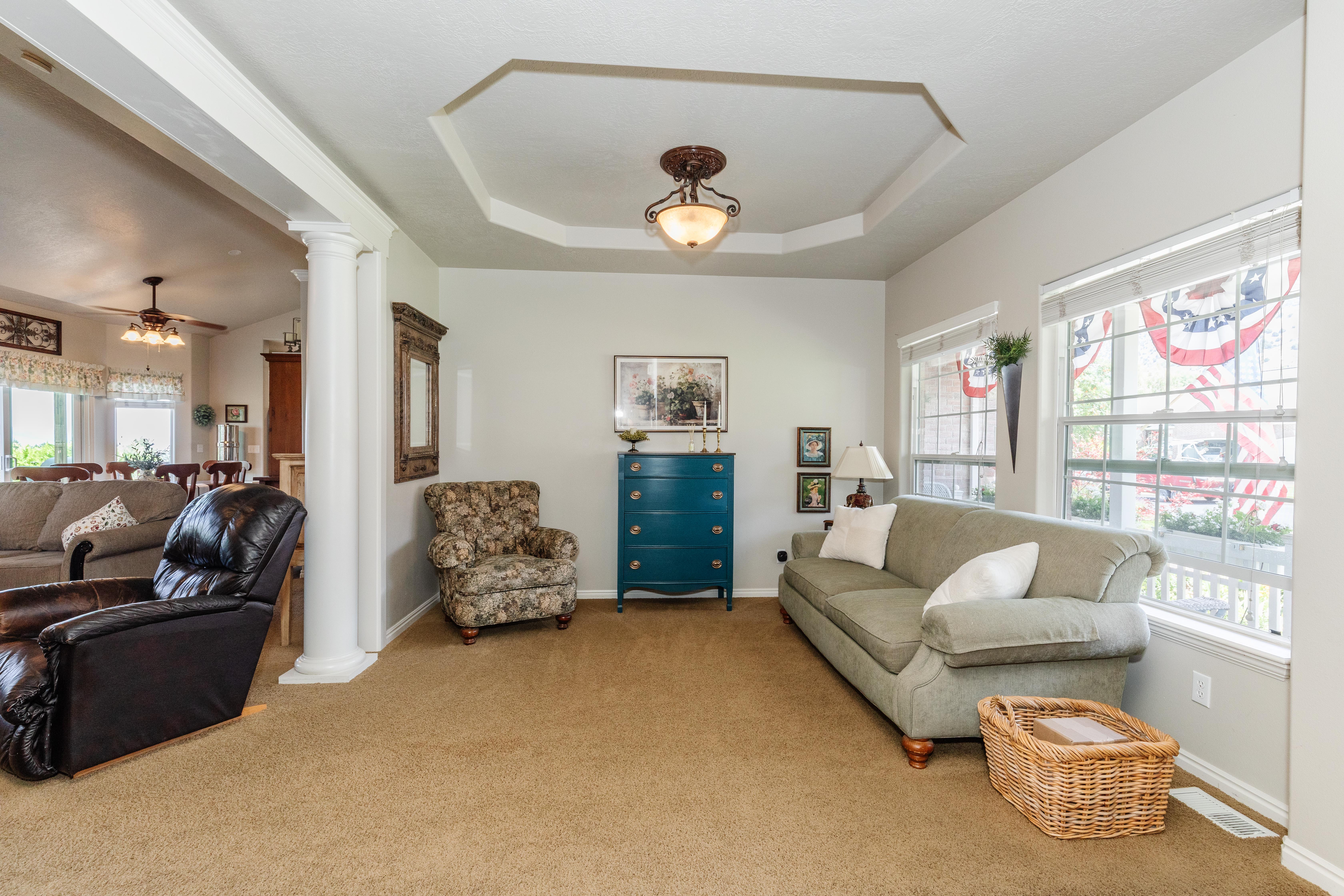 Living area featuring a tray ceiling with a central light fixture, carpeted flooring, and architectural columns