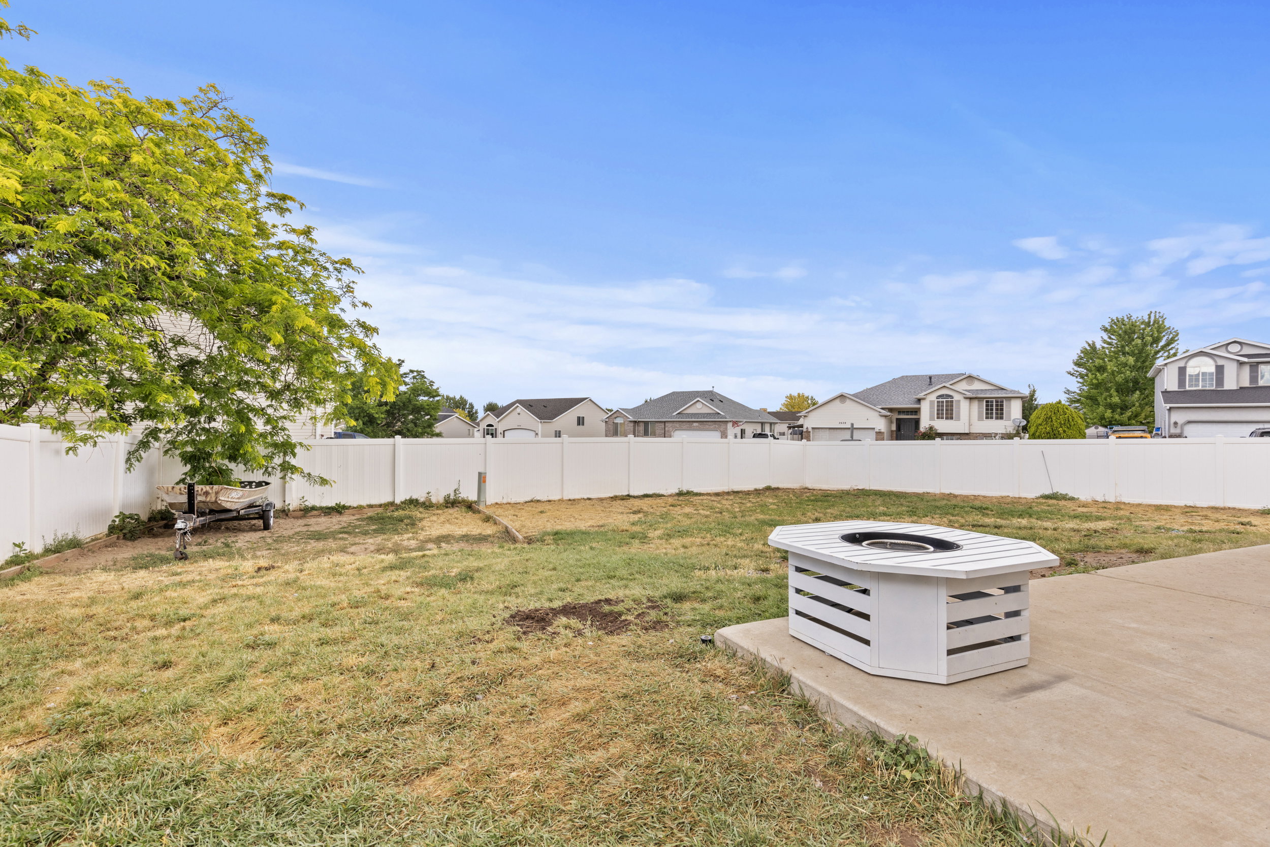 Expansive backyard space featuring a large concrete patio pad, a built-in white fire pit, and a full white vinyl privacy fence