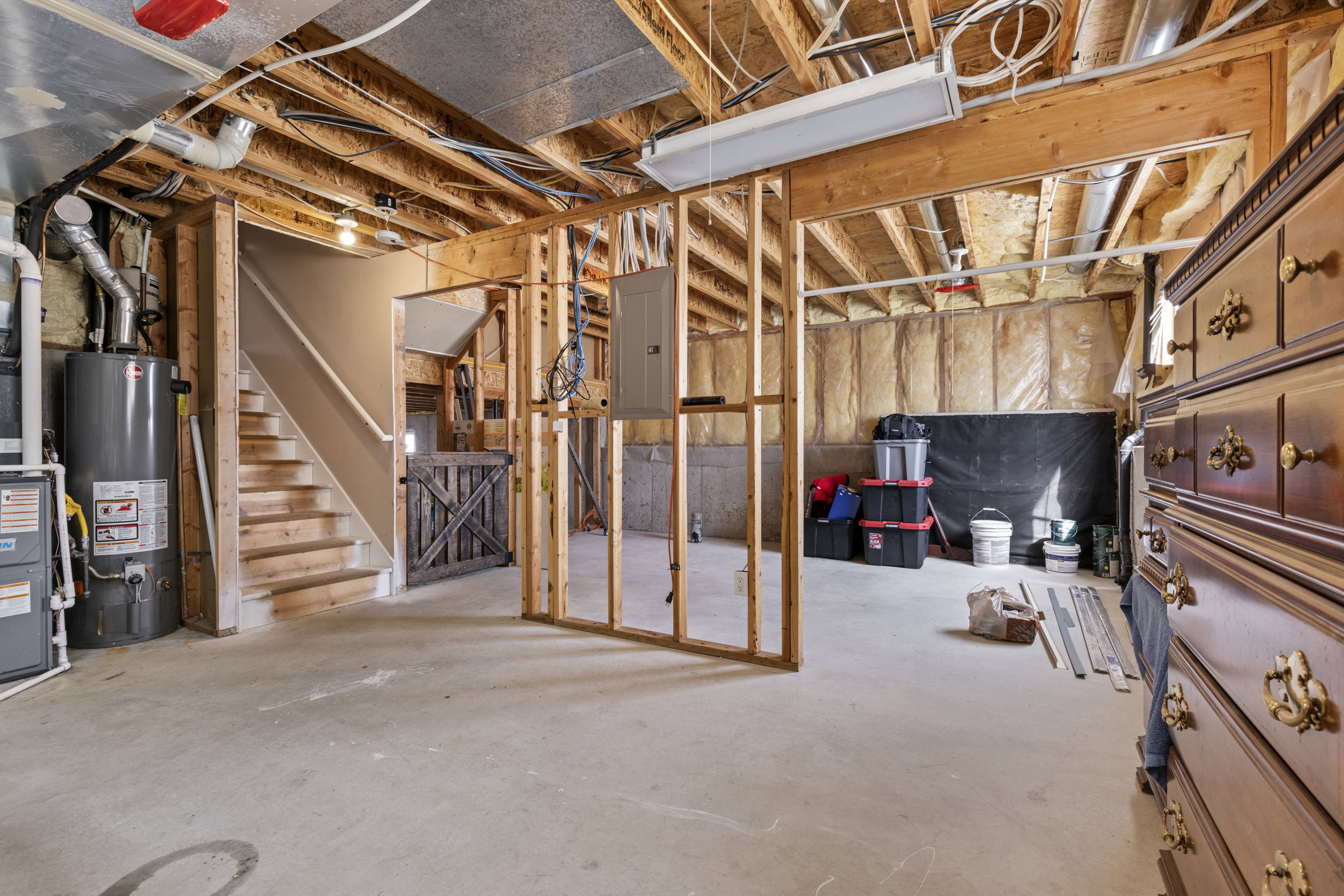 Unfinished basement featuring exposed wood joists, concrete flooring, wood staircase, and framed walls