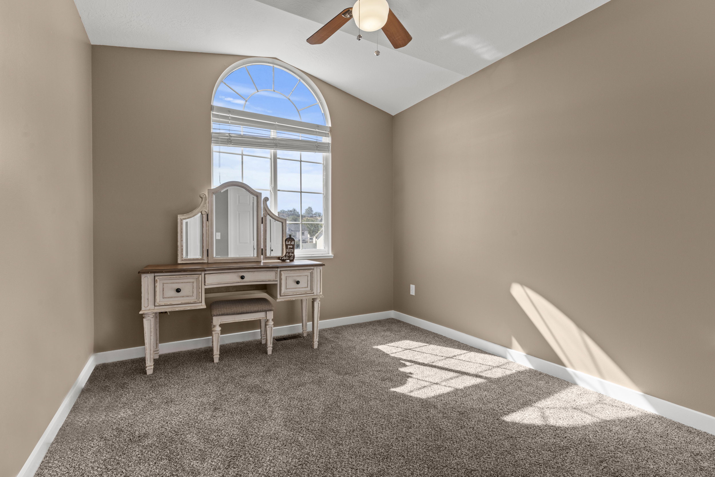 Arched window with upper transom, vaulted ceiling, ceiling fan with integrated lighting, and neutral tone carpeting
