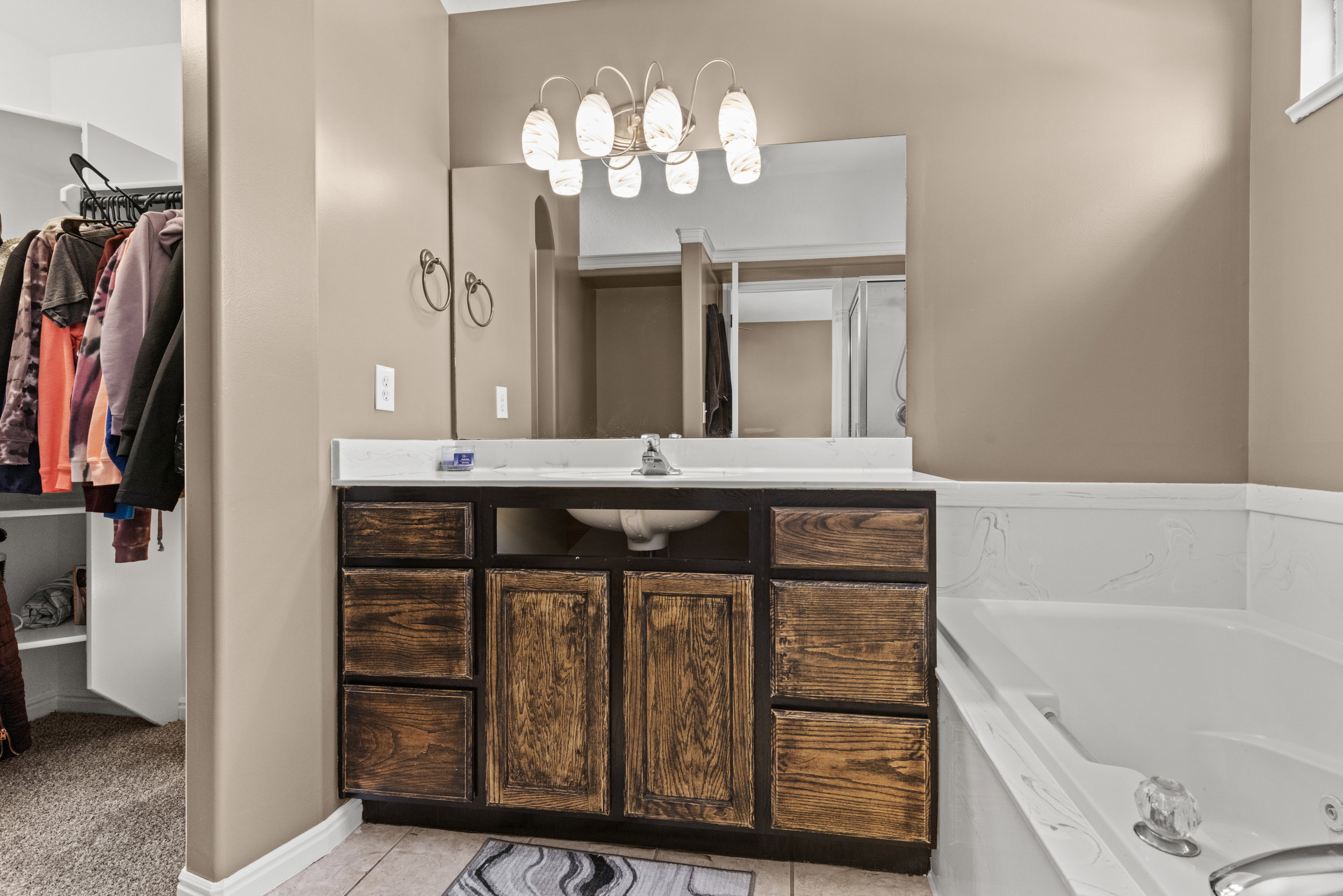 Vanity with a white countertop and integrated sink, framed by a large mirror and illuminated by an overhead light fixture