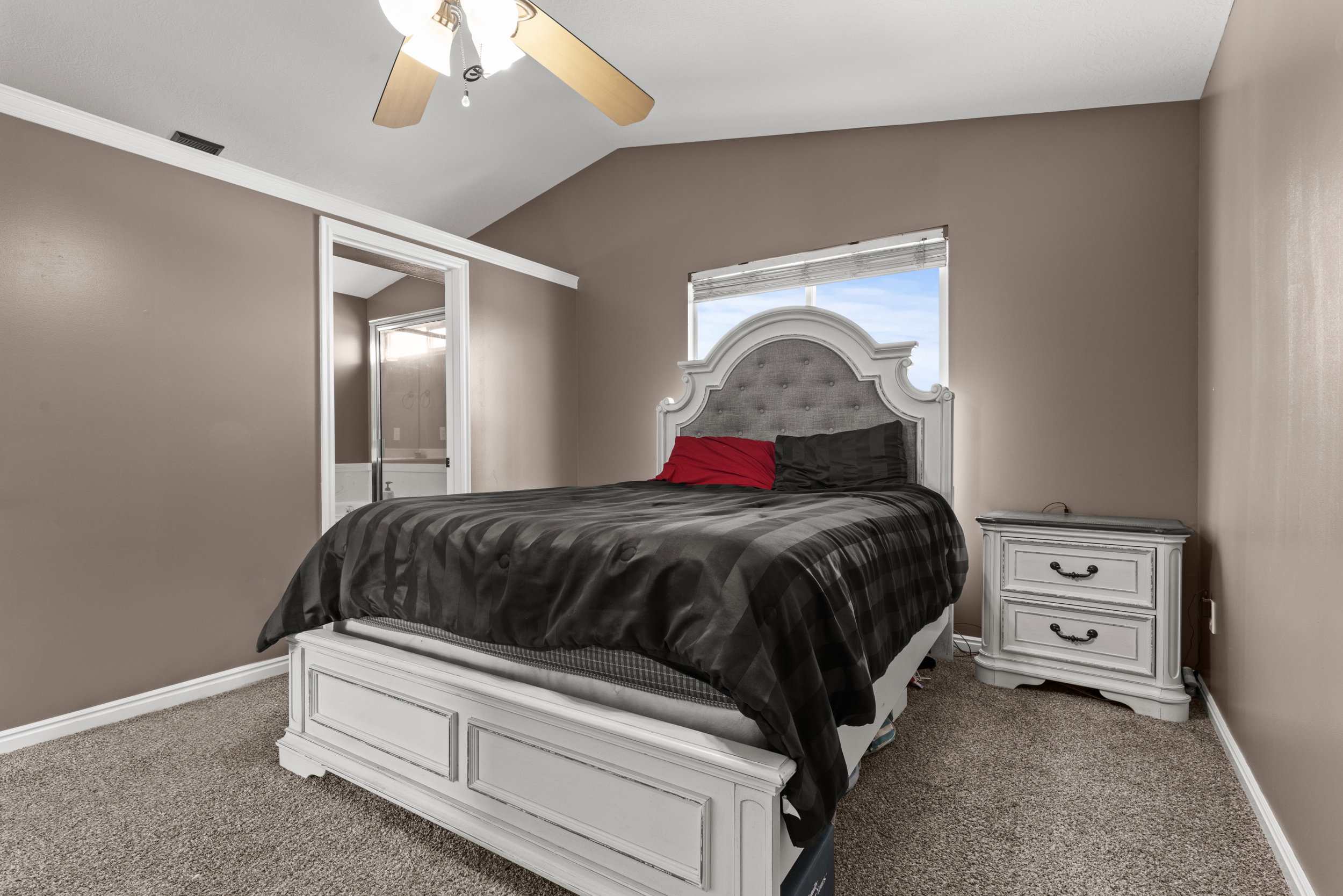 Carpeted bedroom featuring a vaulted ceiling with a ceiling fan, a window with blinds, and a doorway opening to an interior space