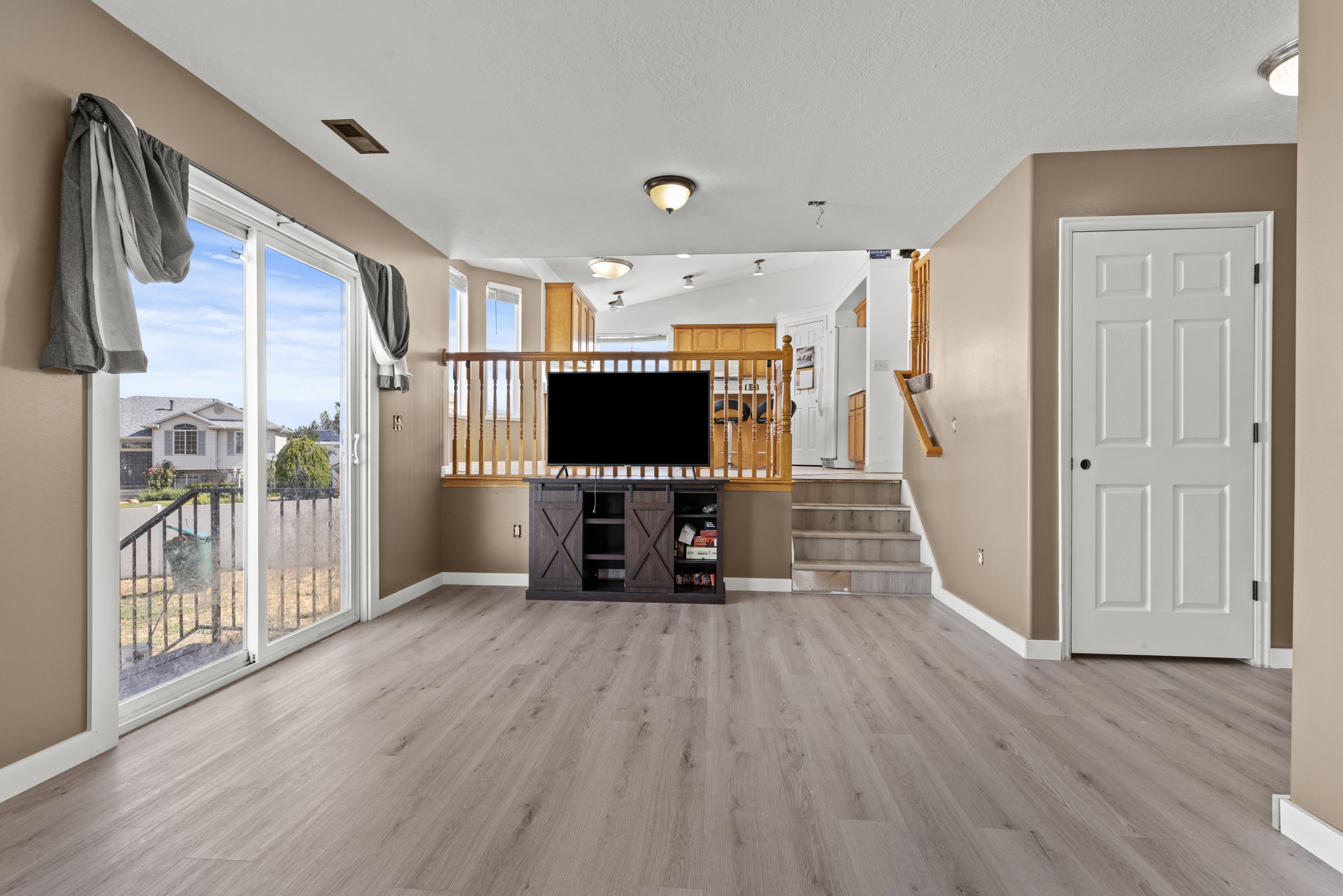 Spacious living area featuring light wood-finish flooring, a neutral wall palette, and a sliding glass door