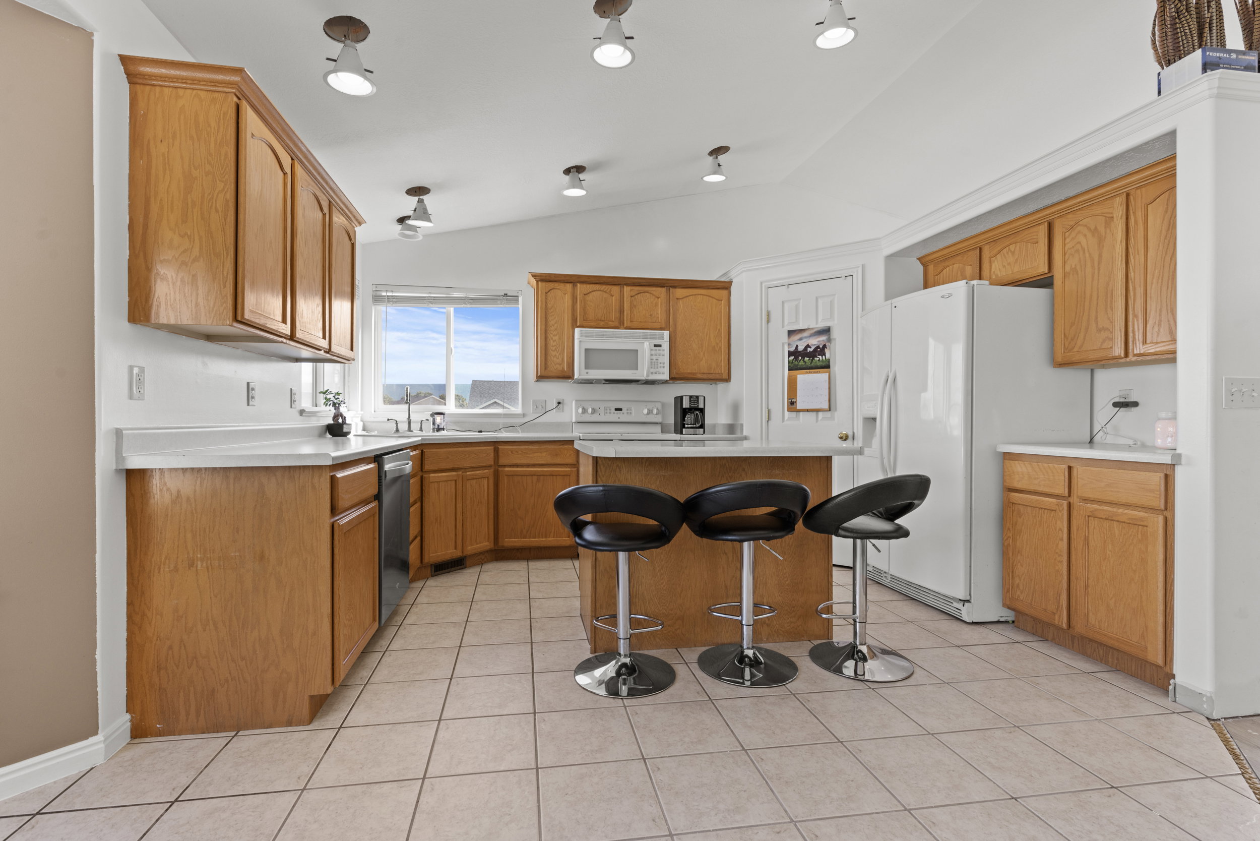 Spacious kitchen featuring extensive cabinetry, an island with seating, tile flooring, white countertops, and a window for natural light