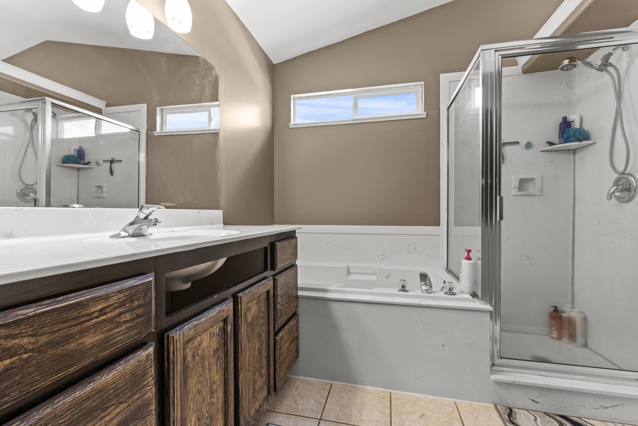 Bathroom featuring a wood-finish vanity with a white countertop, a built-in tub, and a glass-enclosed shower with a chrome shower head