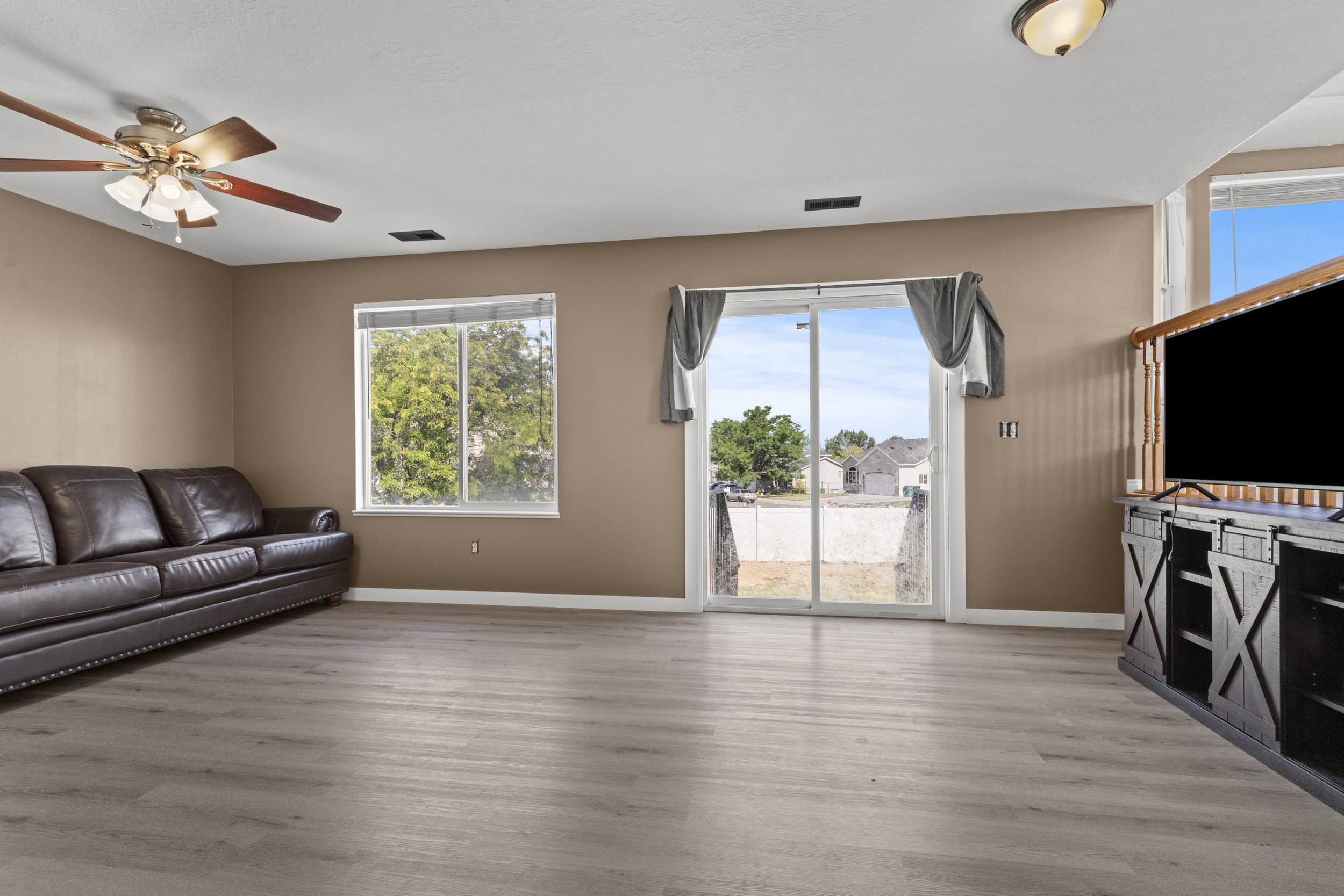 Spacious room featuring wood-finish flooring, a ceiling fan, and earth-toned walls