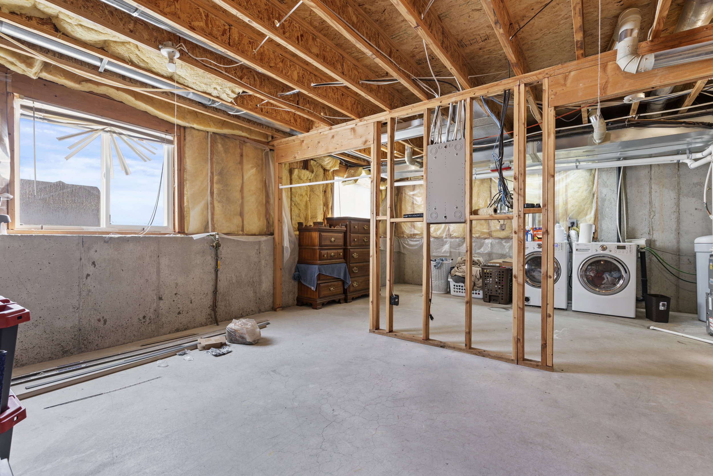 Unfinished basement space featuring exposed wooden ceiling joists, concrete slab flooring, and framed walls