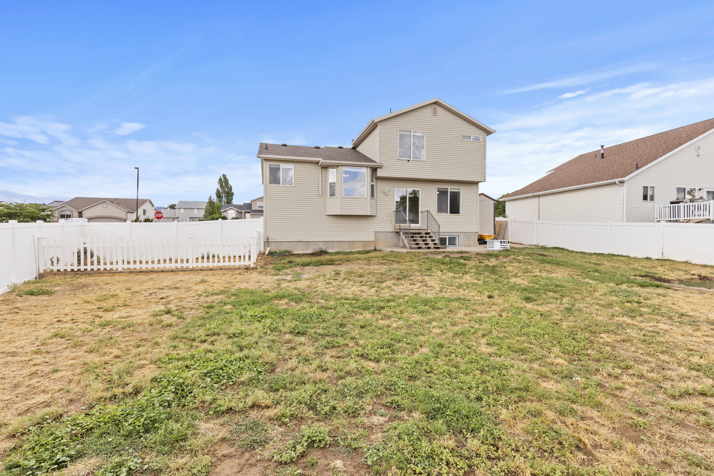 Expansive backyard featuring a white vinyl privacy fence, a white picket fence section, and a full-height house exterior with multiple windows