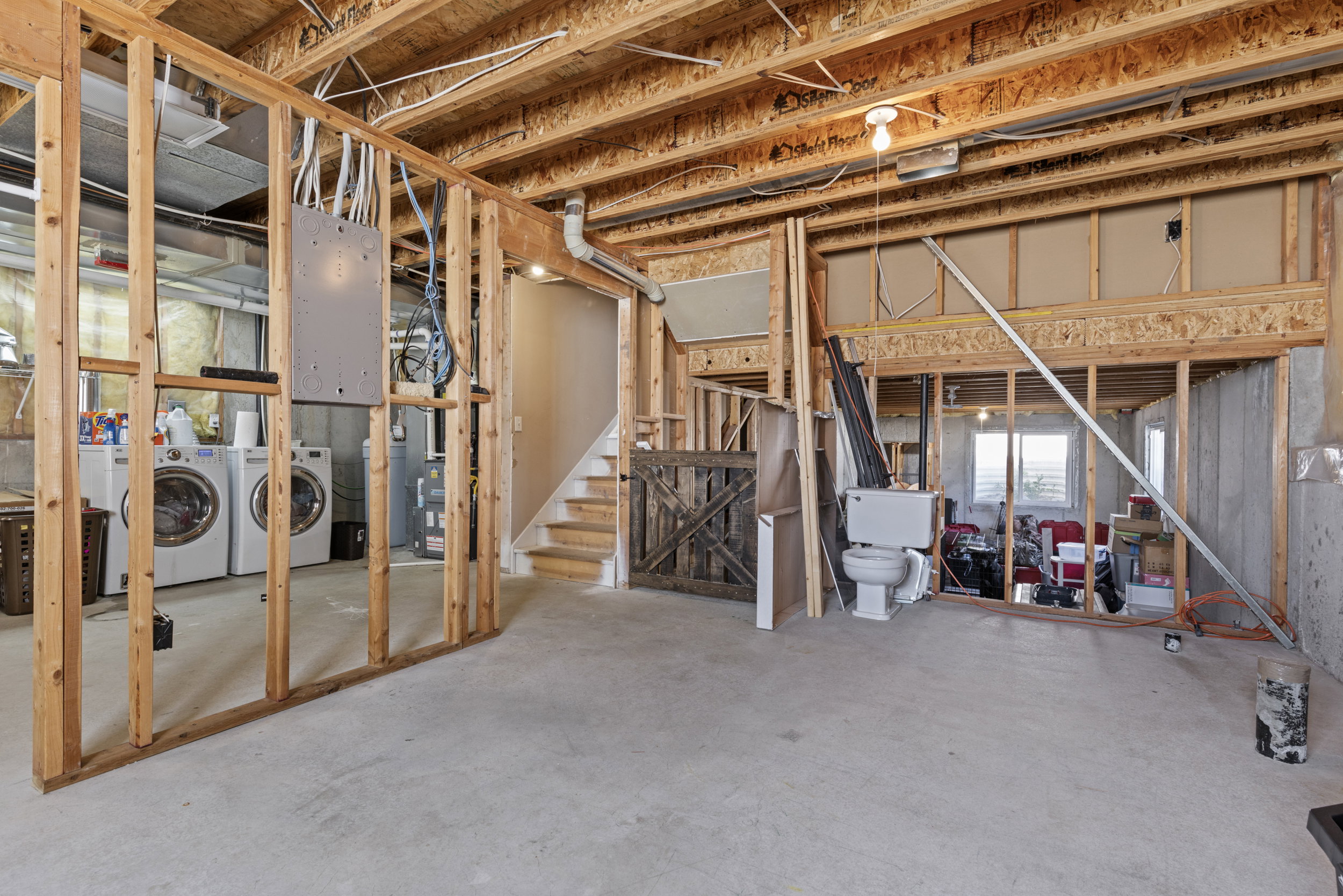 Unfinished basement featuring exposed wood framing, concrete flooring, and a visible electrical panel
