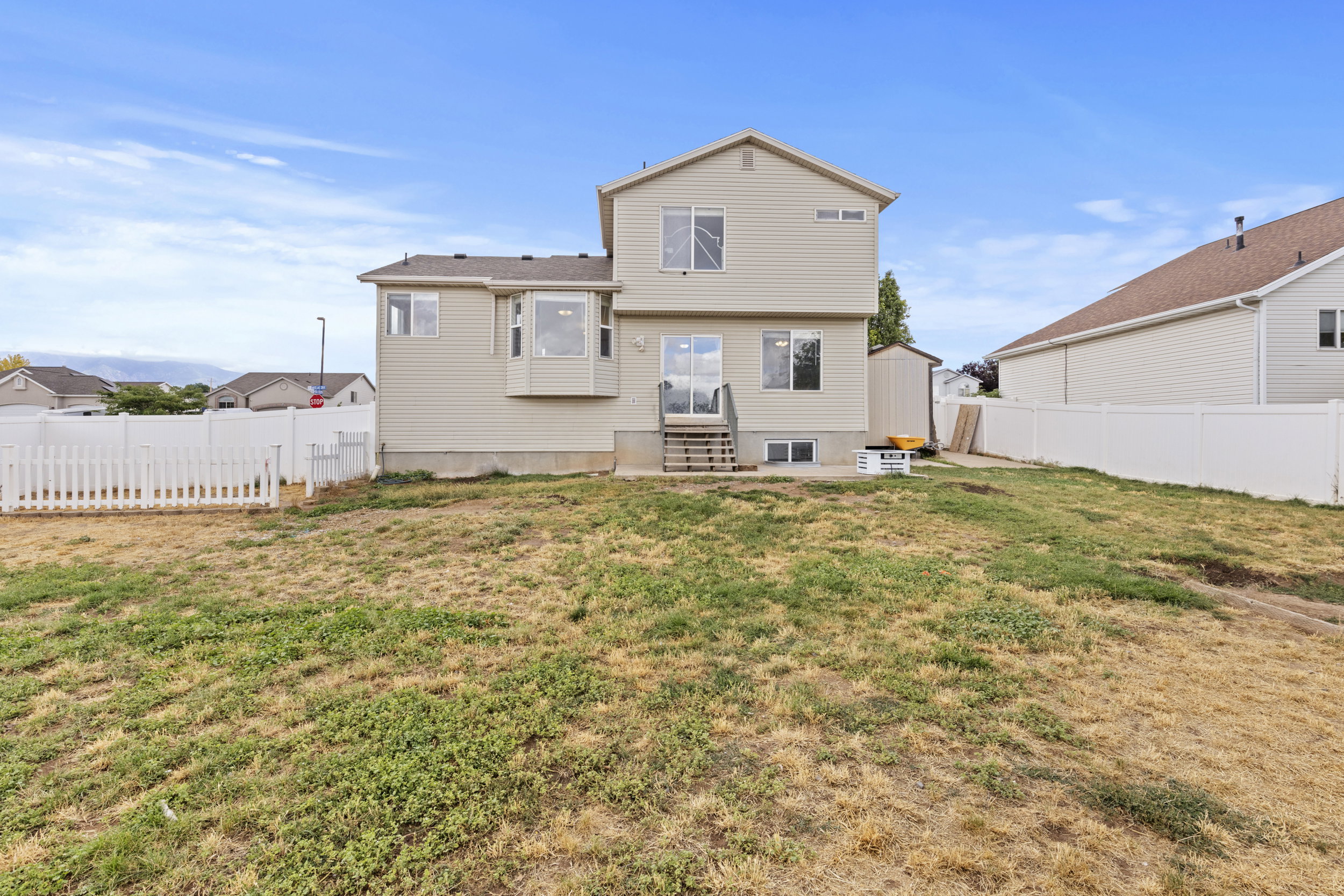 Expansive backyard featuring a white picket fence, a privacy fence, and a storage shed