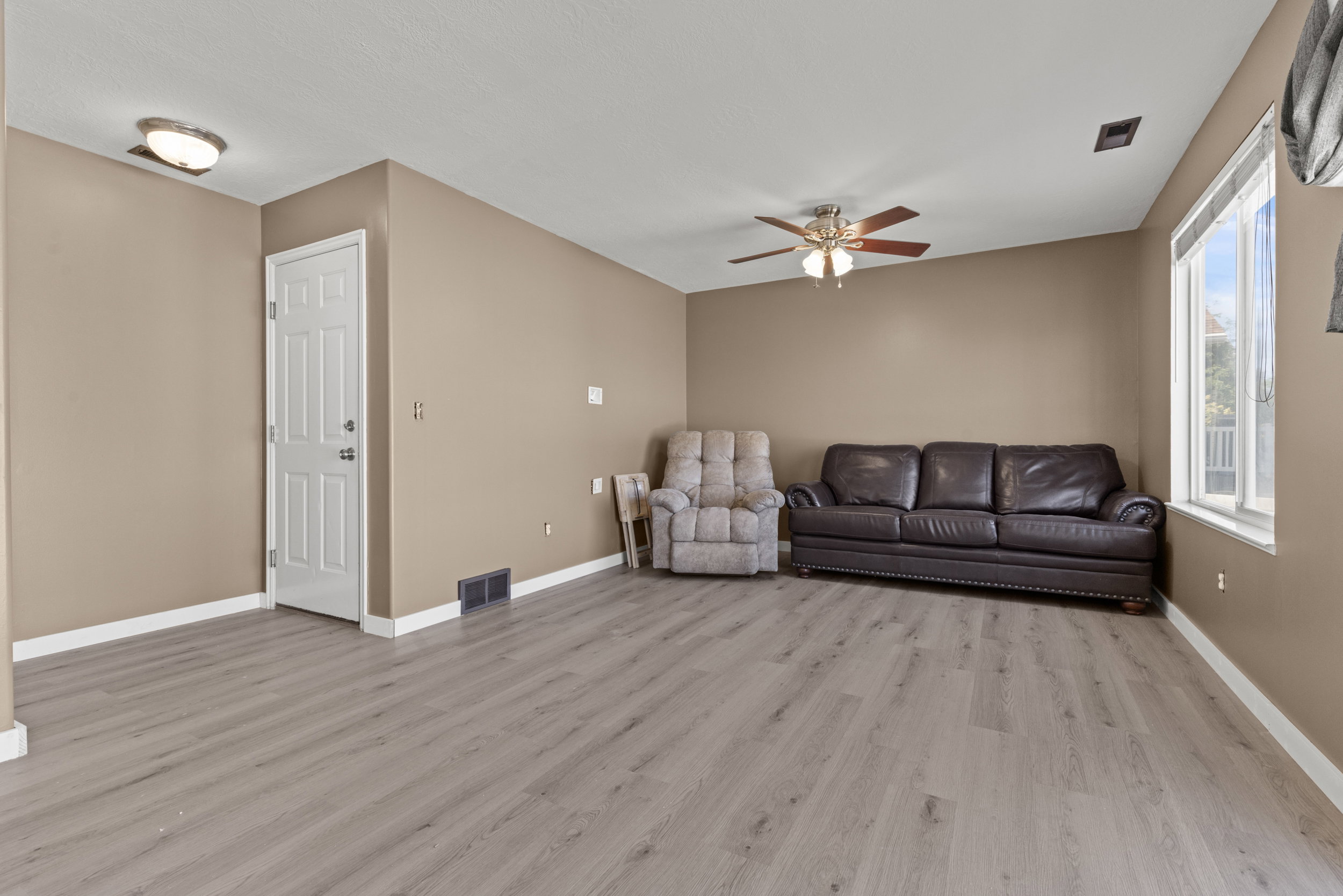 Spacious room featuring light wood-finish flooring, neutral wall tones, a white paneled door, and a multi-pane window