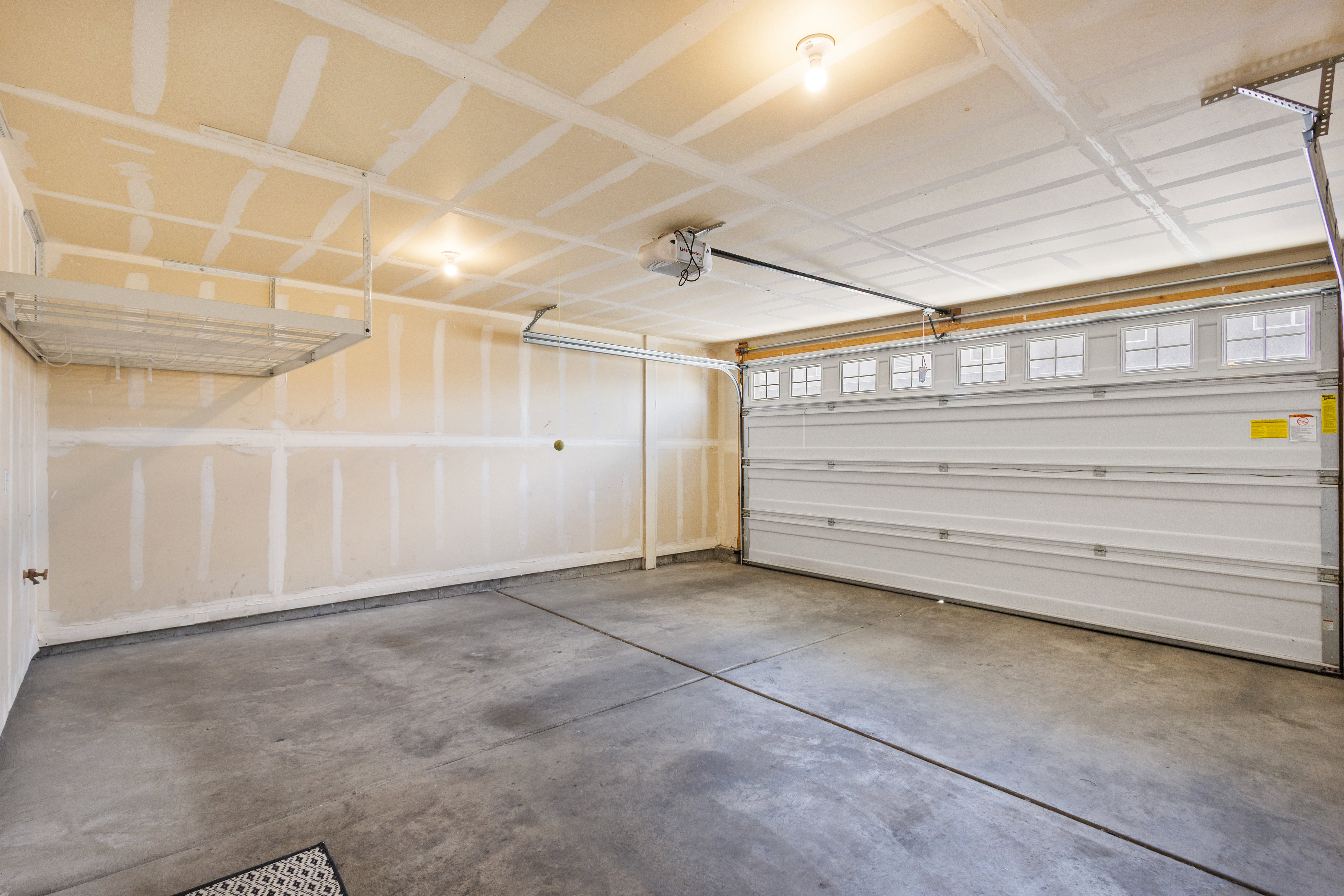 Spacious garage featuring a concrete floor, built-in overhead storage rack, and a white paneled garage door with upper window inserts