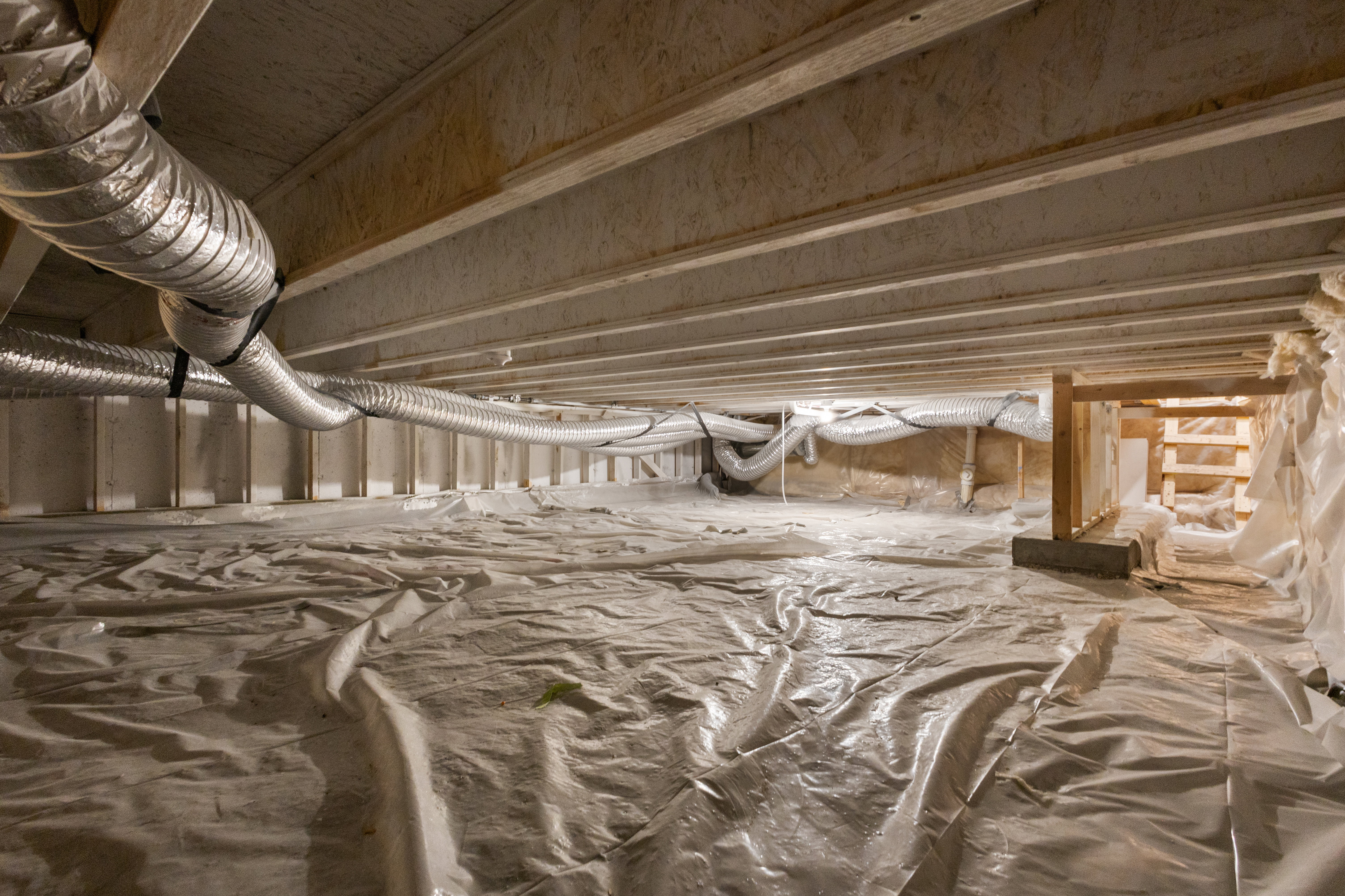Encapsulated crawl space featuring a vapor barrier, visible ductwork, and structural wood framing
