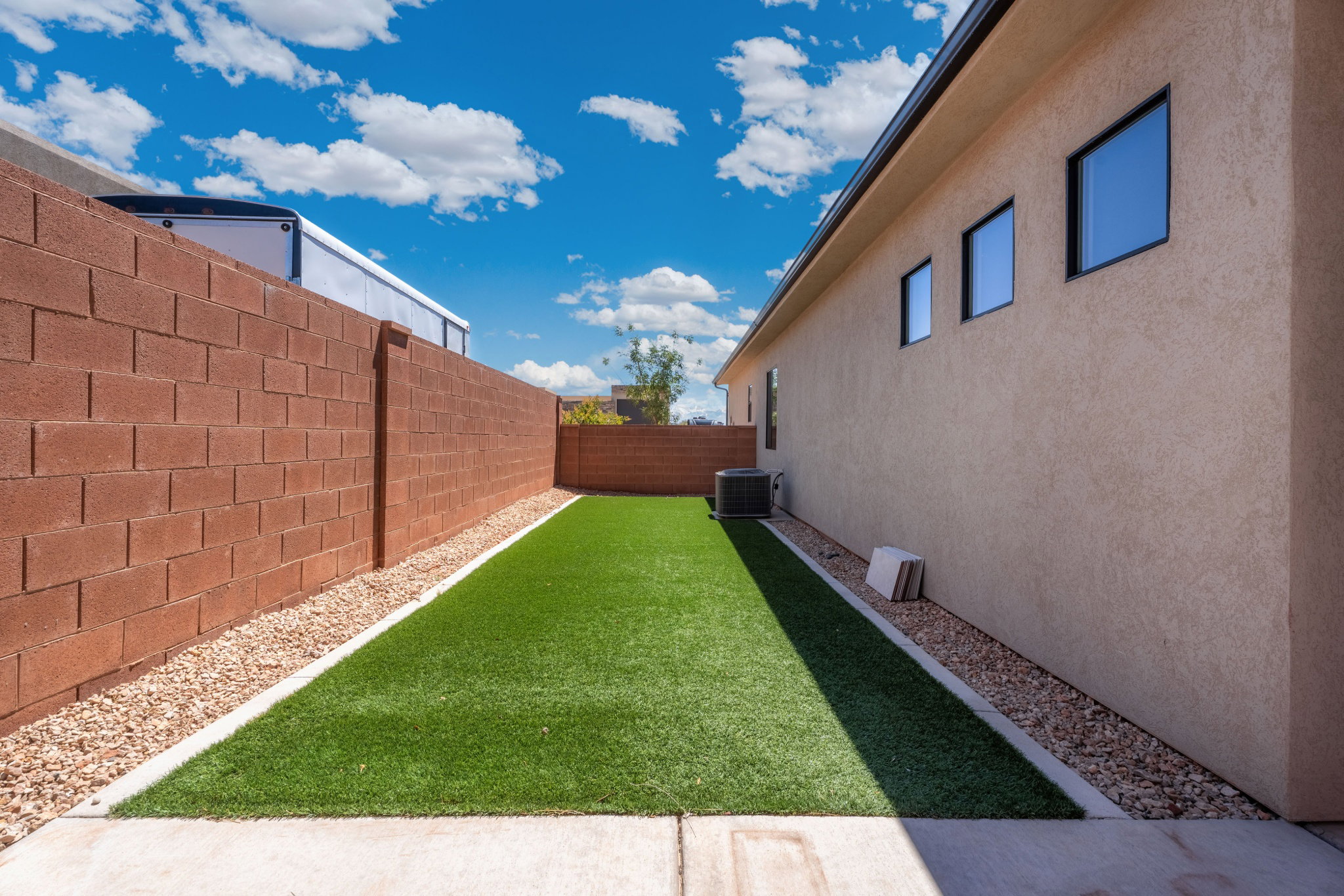 Yard area featuring artificial turf, aggregate stone bordering, and a stucco exterior wall with rectangular windows