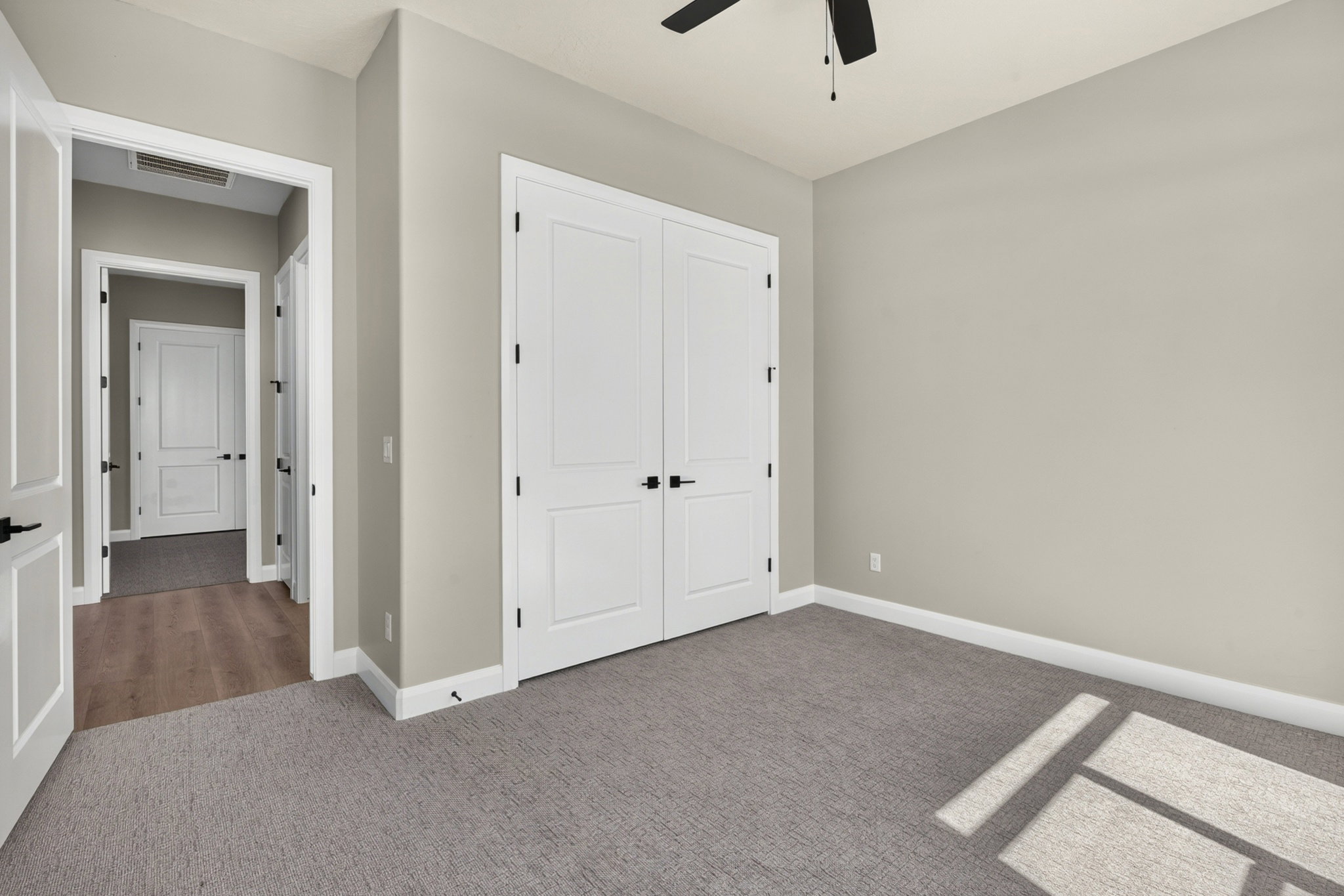 Neutral tone walls with white trim, gray carpet, white panel doors with matte black hardware, and a ceiling fan
