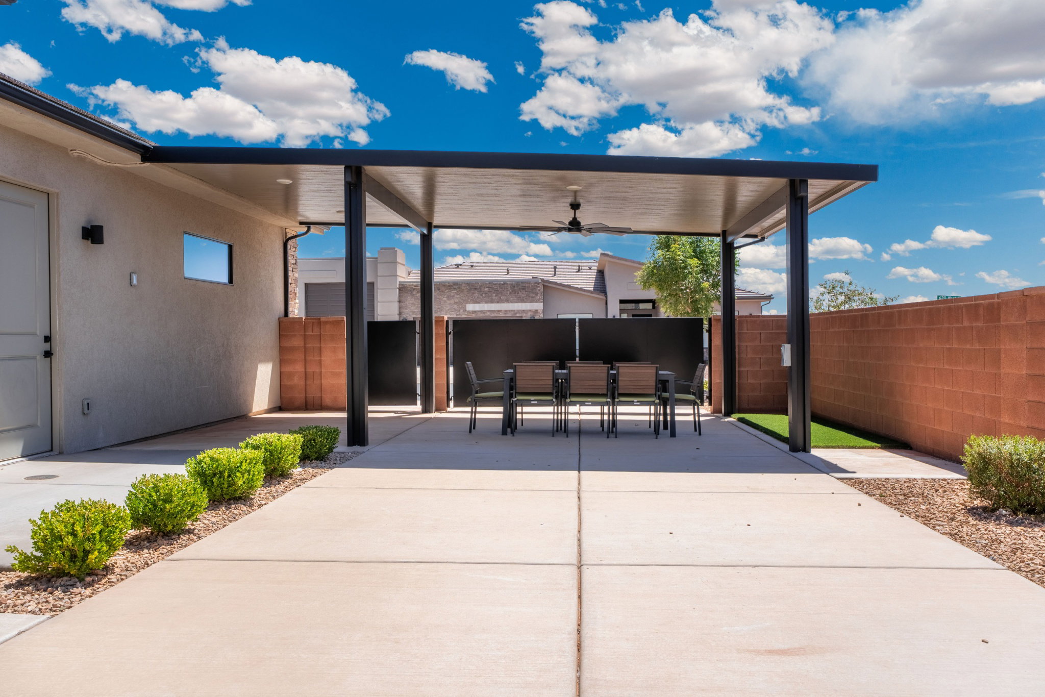 Covered patio with integrated ceiling fan, concrete paver flooring, low-maintenance landscaping, and surrounding block wall