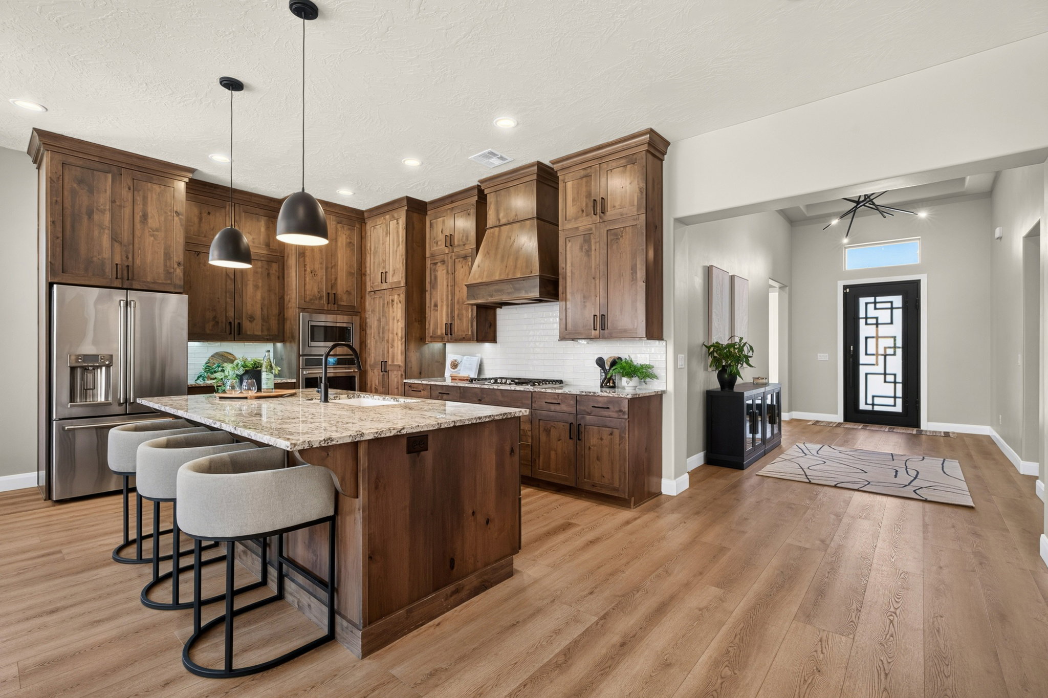 Gourmet kitchen featuring a substantial island with stone countertop, stainless steel appliances, wood-finish cabinetry, a subway tile backsplash, and contemporary pendant lighting