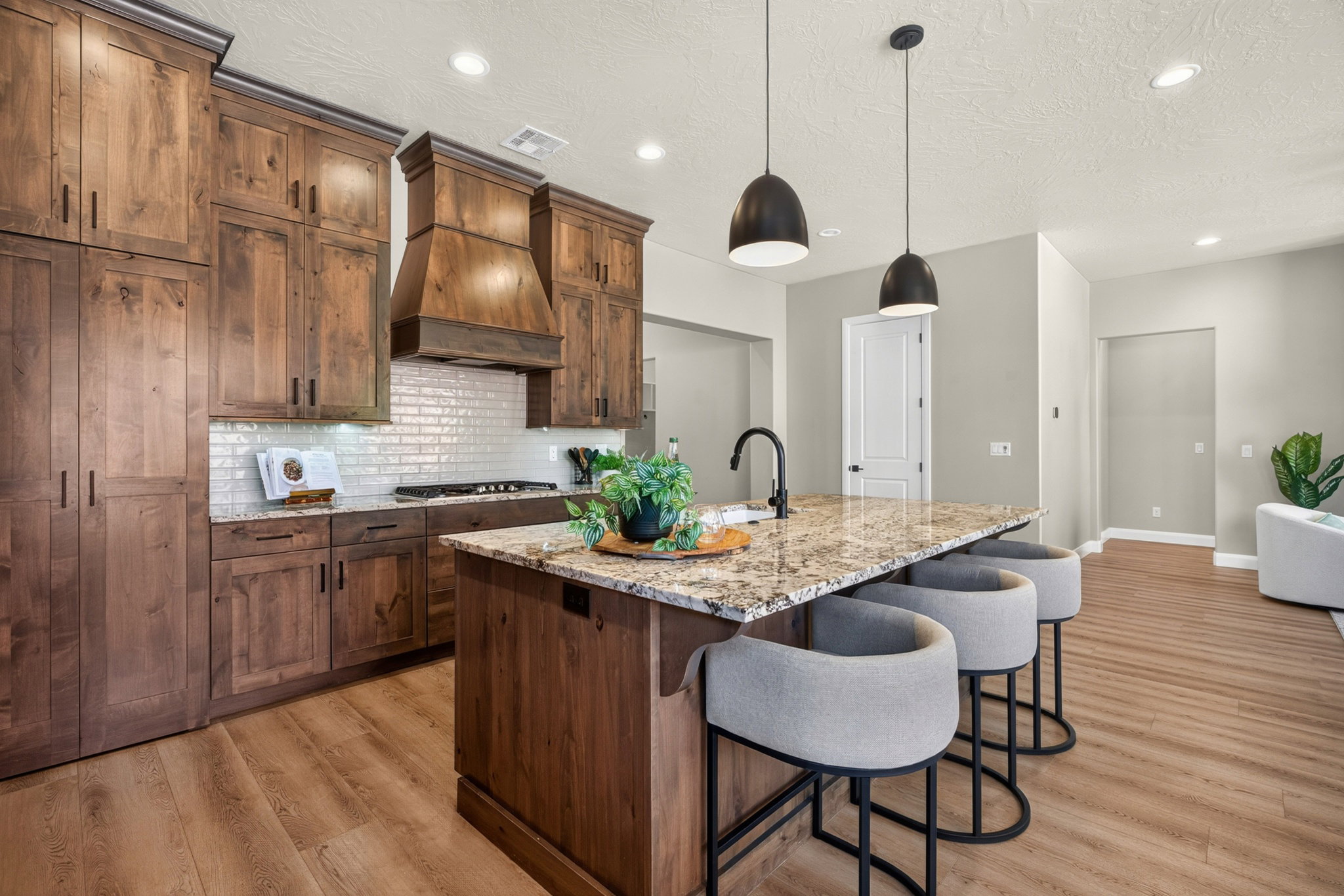 Gourmet kitchen featuring a substantial island with seating, granite countertops, wood-finish flooring, custom wood cabinetry, and a subway tile backsplash