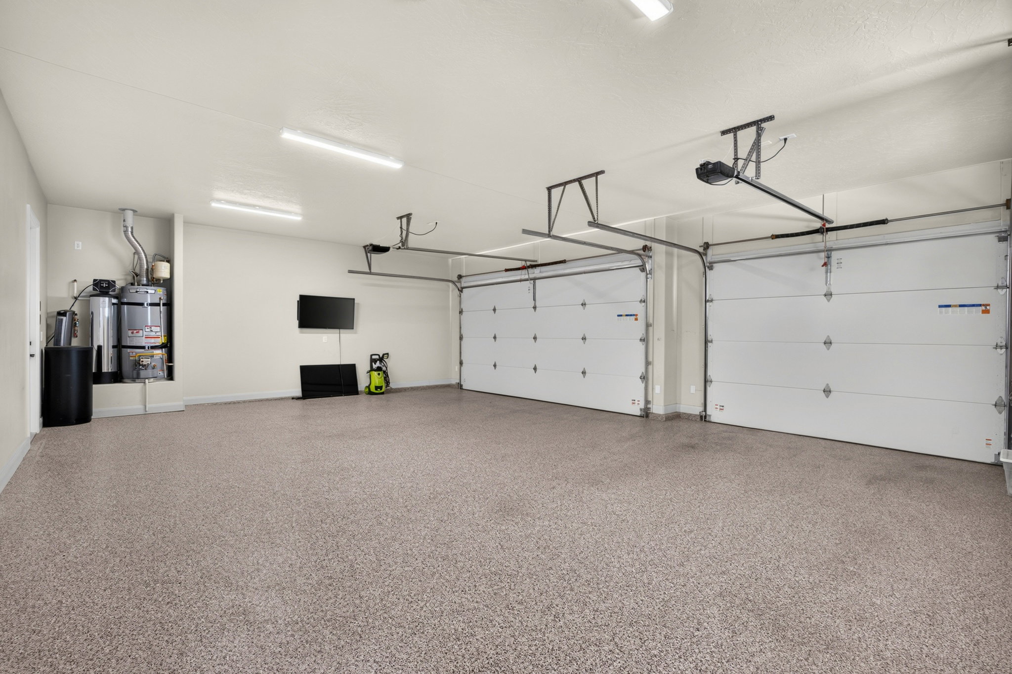 Two-car garage featuring a speckled epoxy floor coating, two overhead garage doors with automatic openers, wall-mounted water heater, and fluorescent overhead lighting