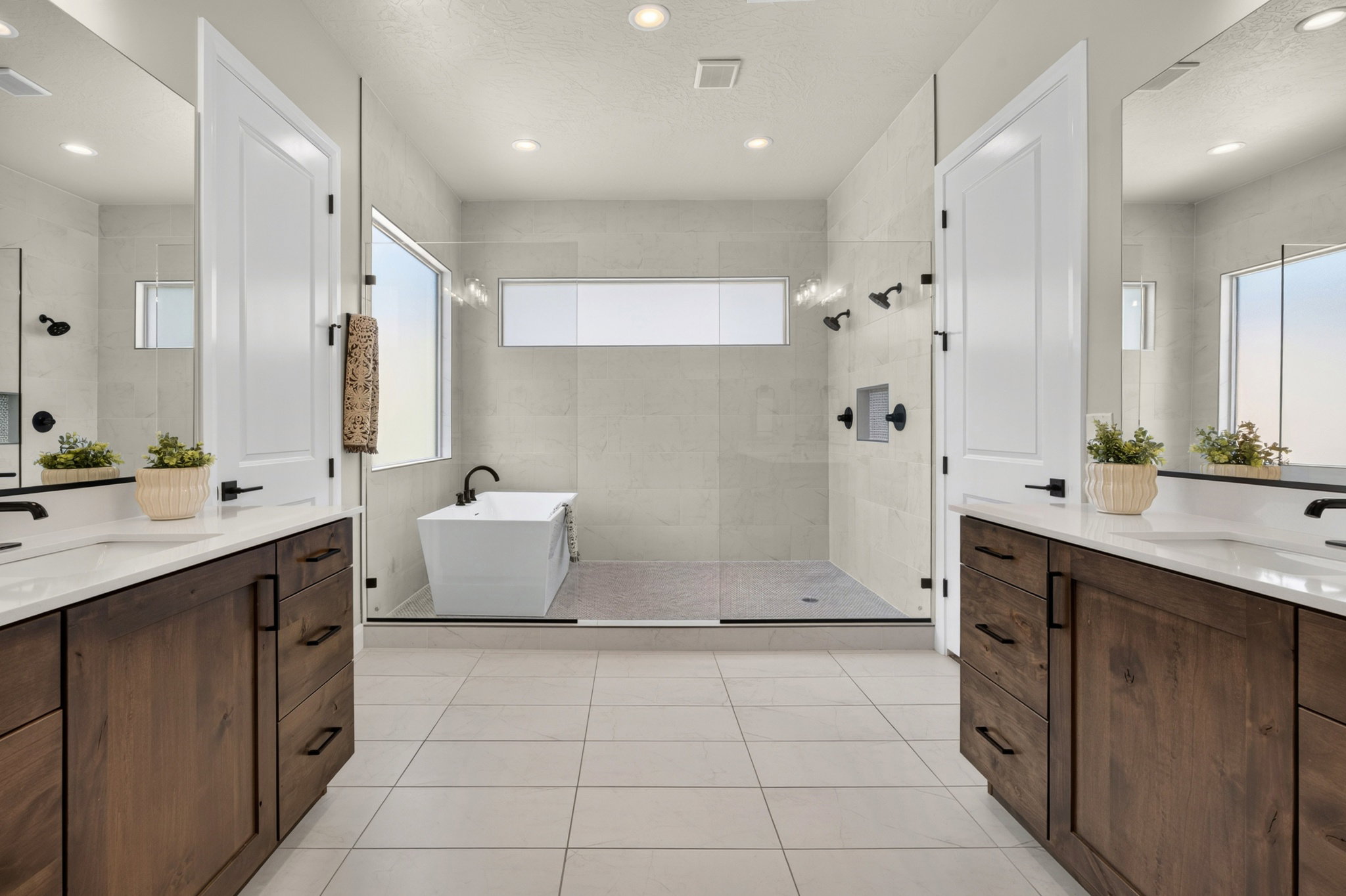 Contemporary bathroom featuring dual wood-finish vanities with quartz countertops and undermount sinks, a freestanding soaking tub, a spacious glass-enclosed shower with multiple showerheads, and recessed lighting