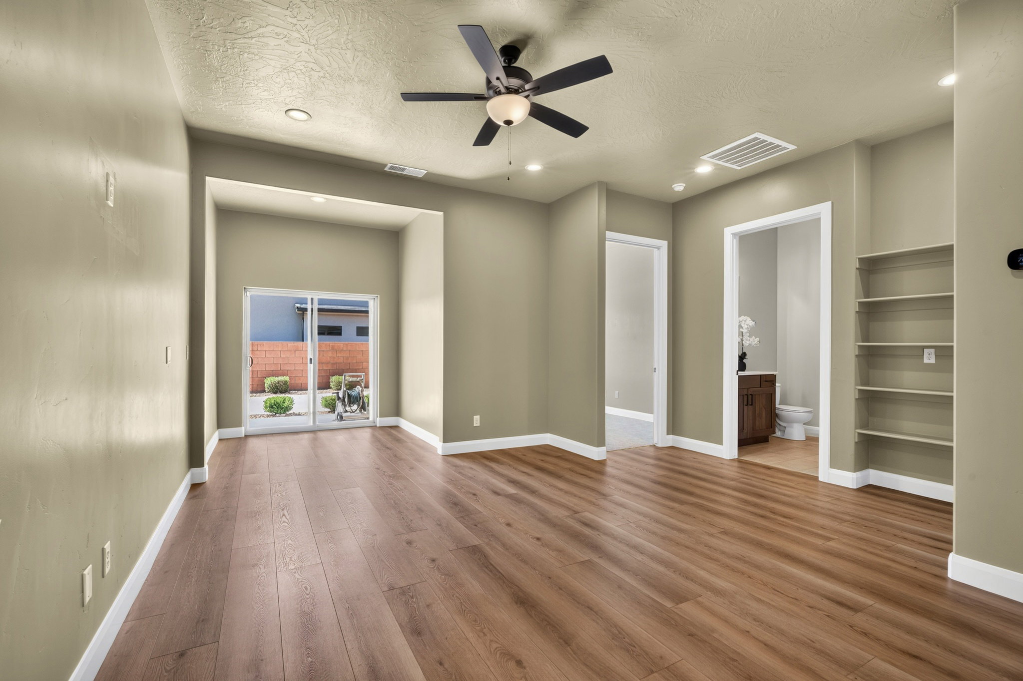 Spacious interior featuring wood-finish flooring, a ceiling fan with integrated lighting, recessed lighting, and built-in shelving