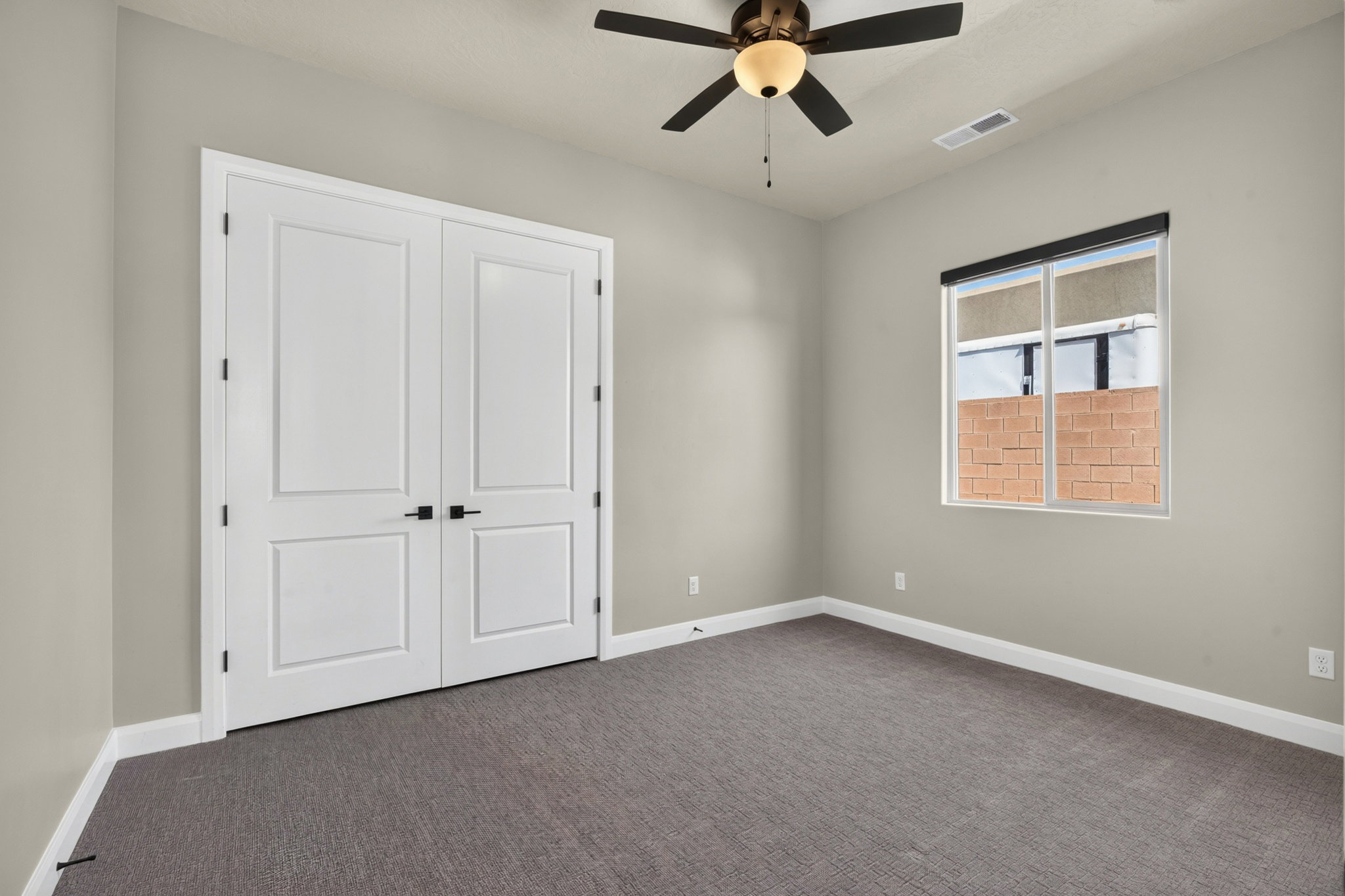 Double panel doors with matte black hardware, gray textured carpeting, and a ceiling fan with light fixture