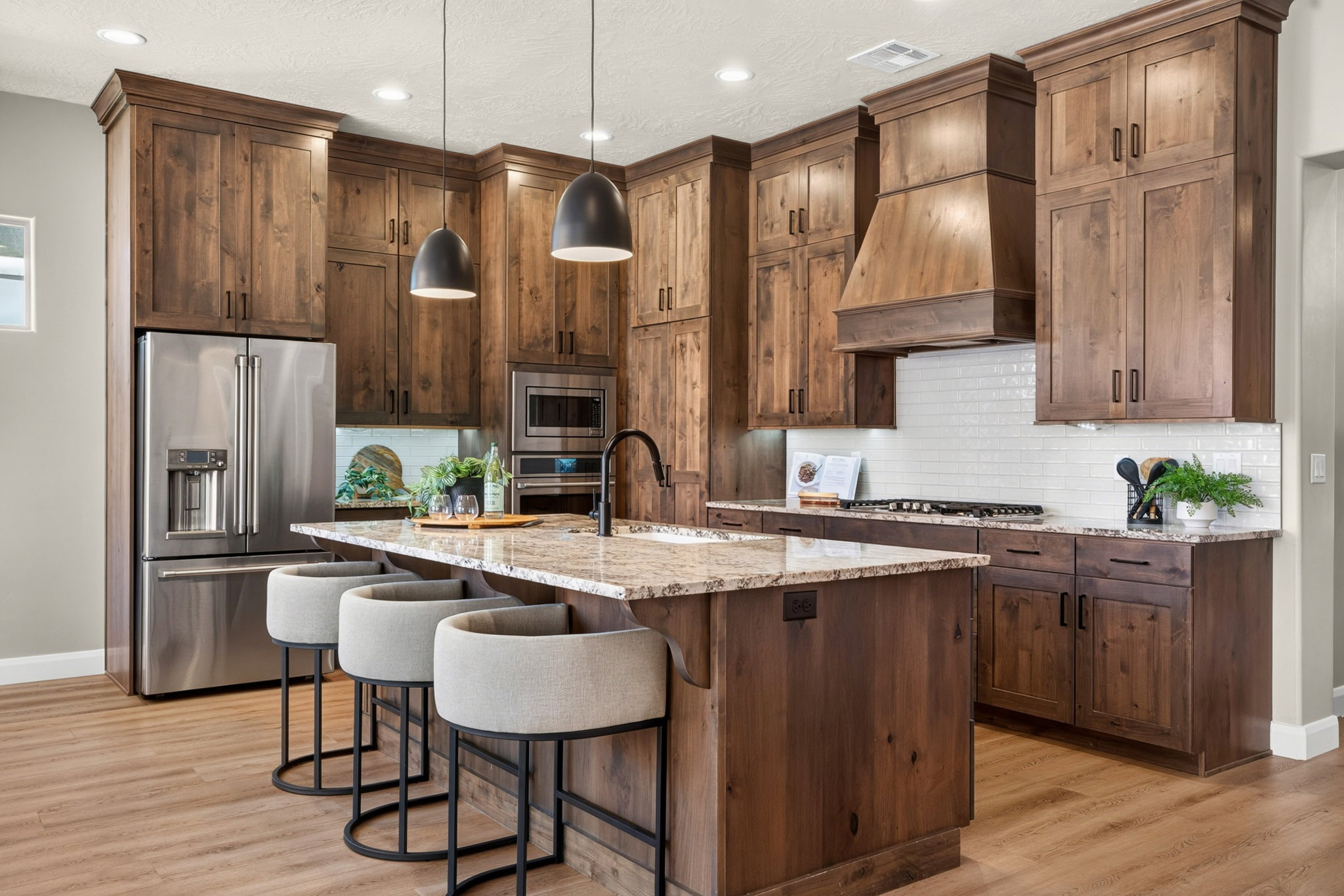 Expansive kitchen featuring wood-finish cabinetry, a large center island with a stone countertop, a tile backsplash, stainless steel appliances, and wood-finish flooring