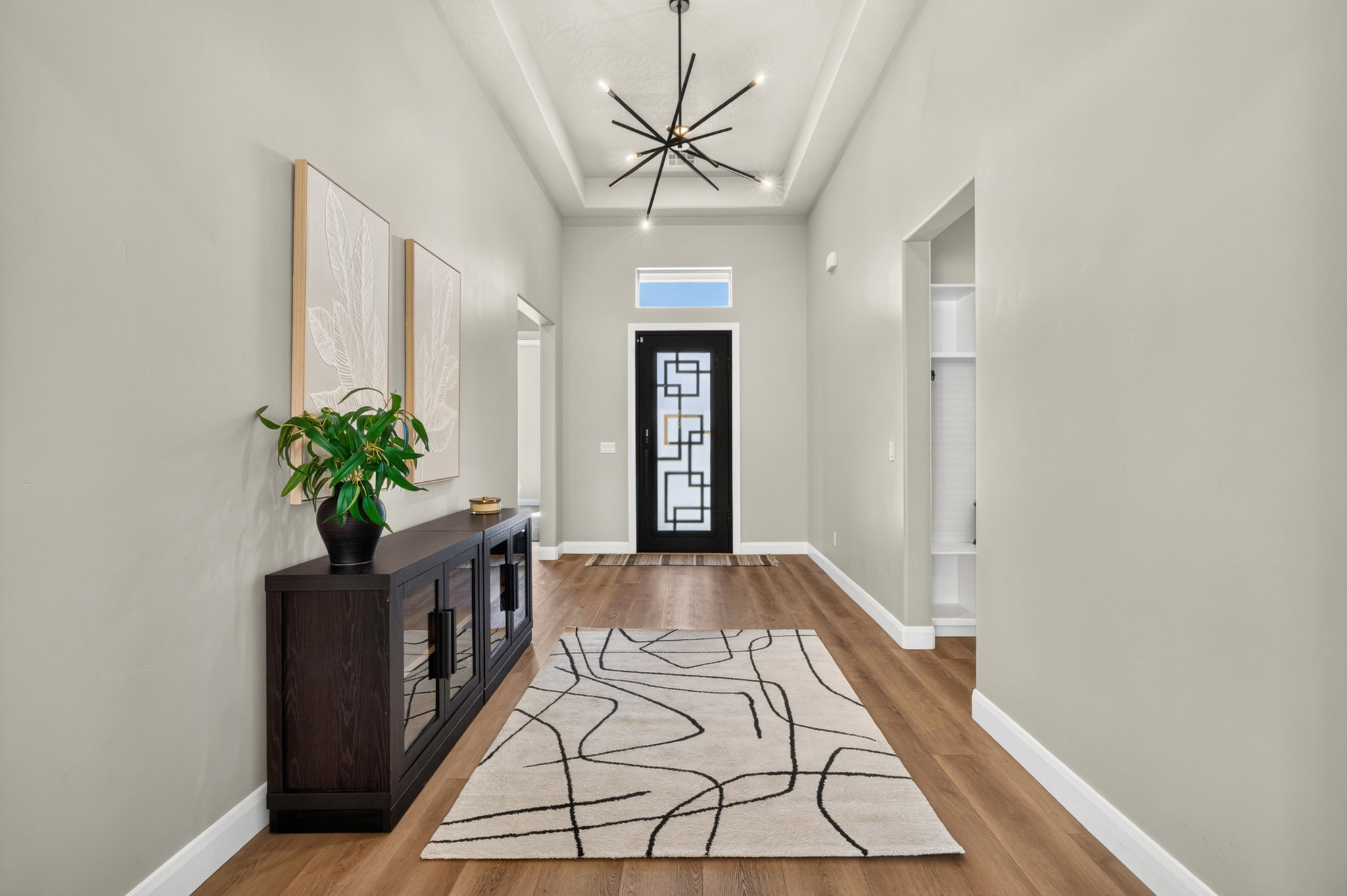 Entryway featuring wood-finish flooring, a contemporary black entry door with decorative glass, and a modern chandelier