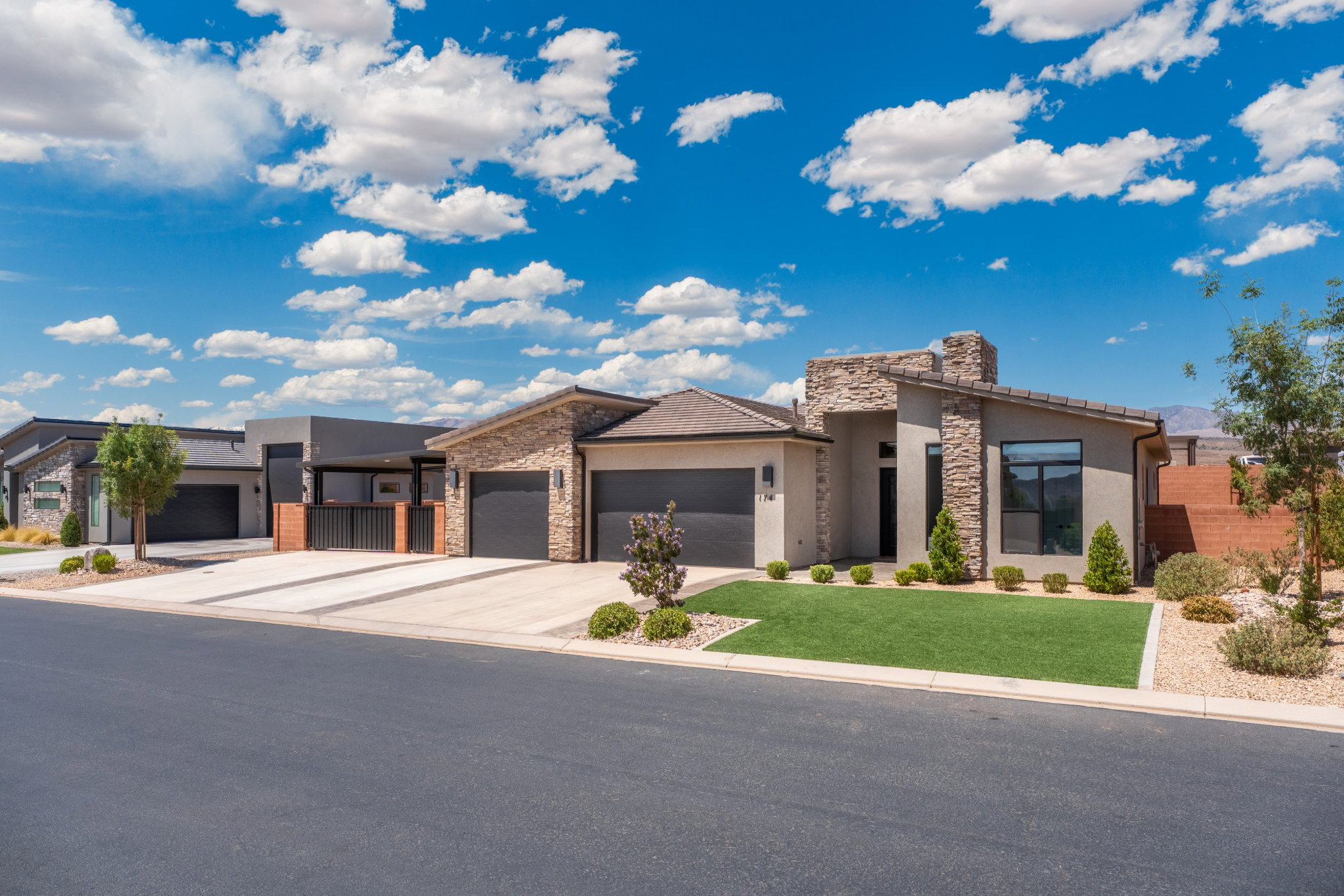 Contemporary stucco exterior featuring stone accents, a low-sloped roofline, a two-car garage, and a manicured front lawn with desert landscaping