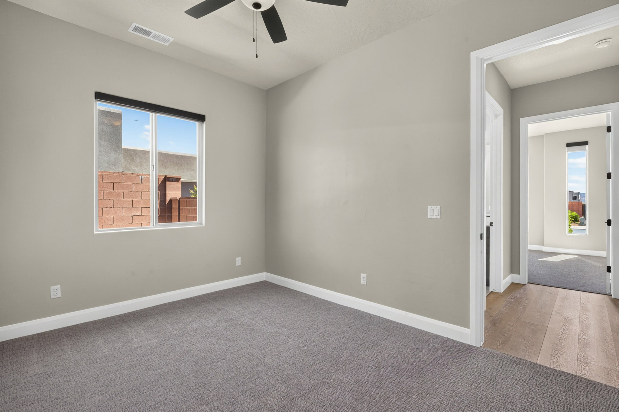 Carpeted room with a ceiling fan and a window featuring a roller shade