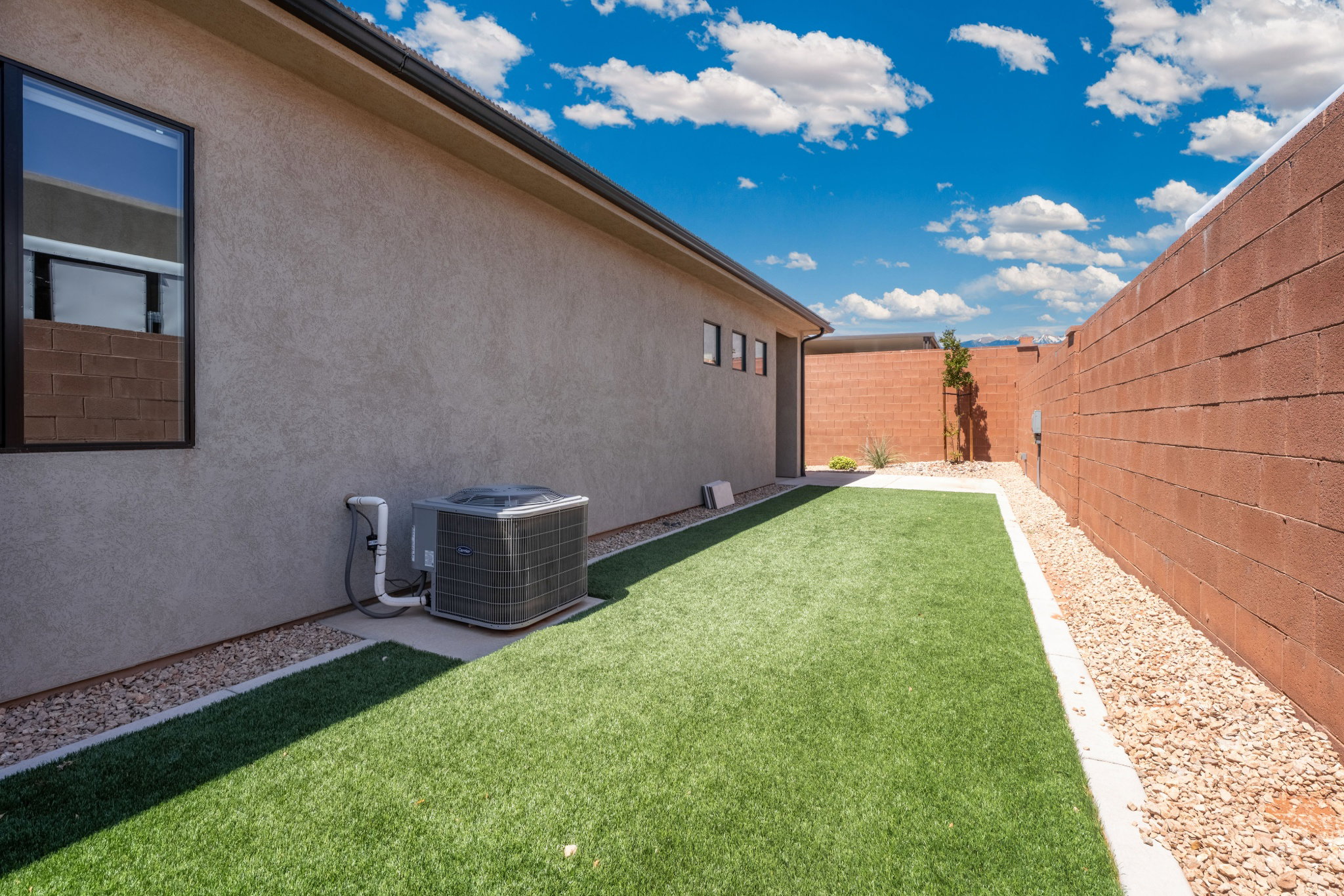 Side yard featuring artificial turf, a rock bed border, and a block wall perimeter