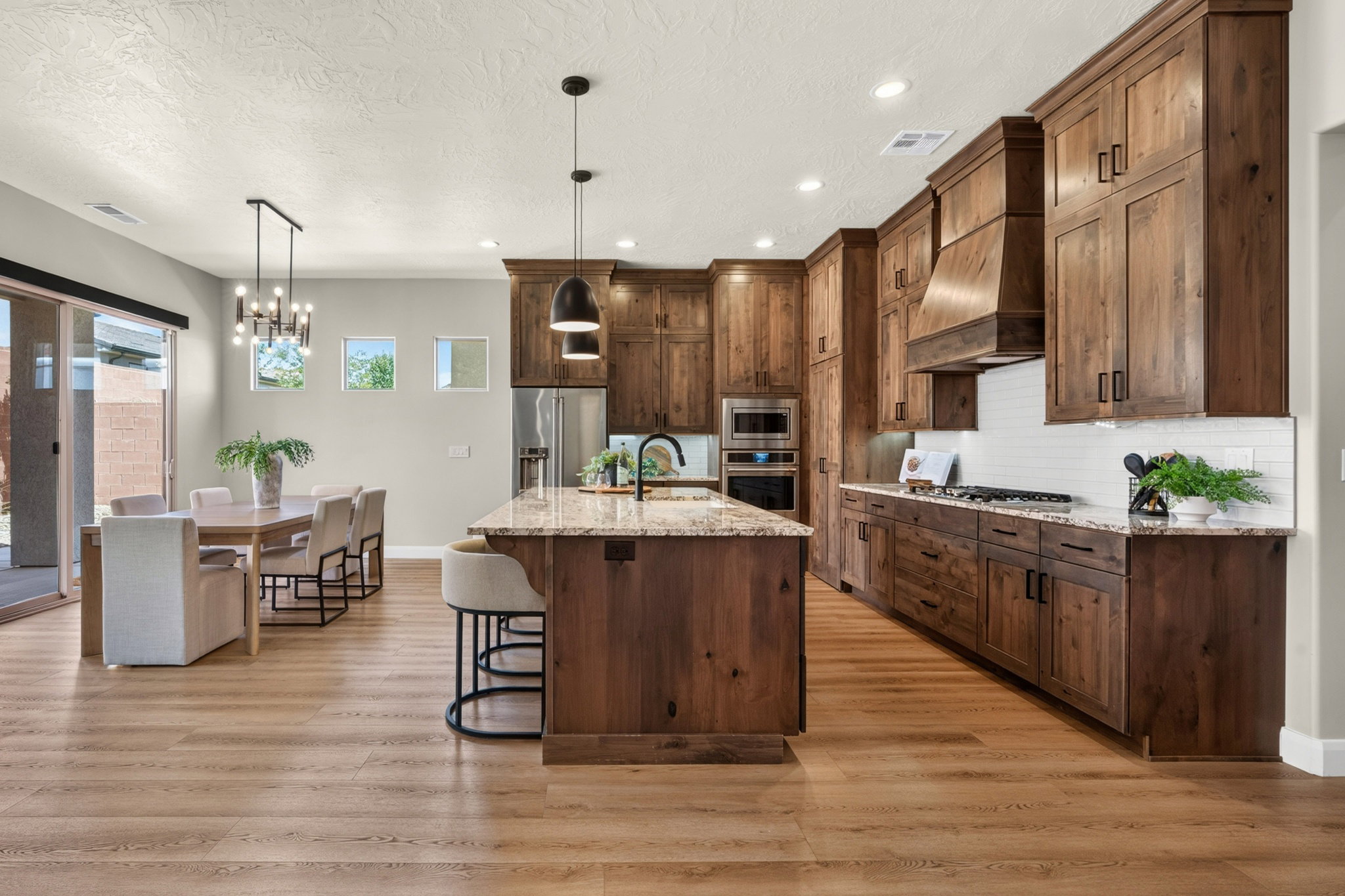 Open-concept kitchen and dining area featuring warm wood-finish cabinetry, light-colored wood-finish flooring, and a large central island with bar seating